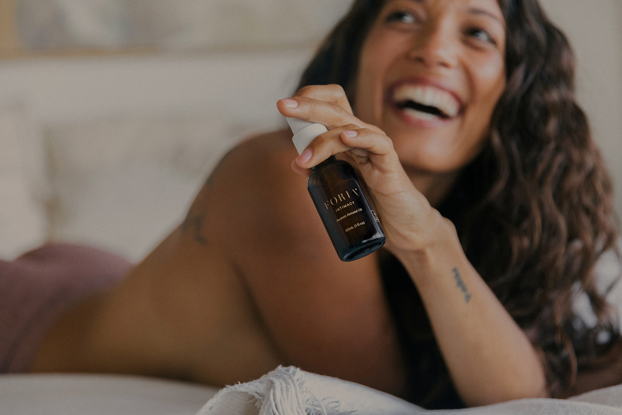 Person smiling and holding a small bottle while lying on a bed.