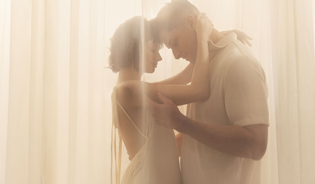 A couple embracing softly in a warm, softly lit setting.