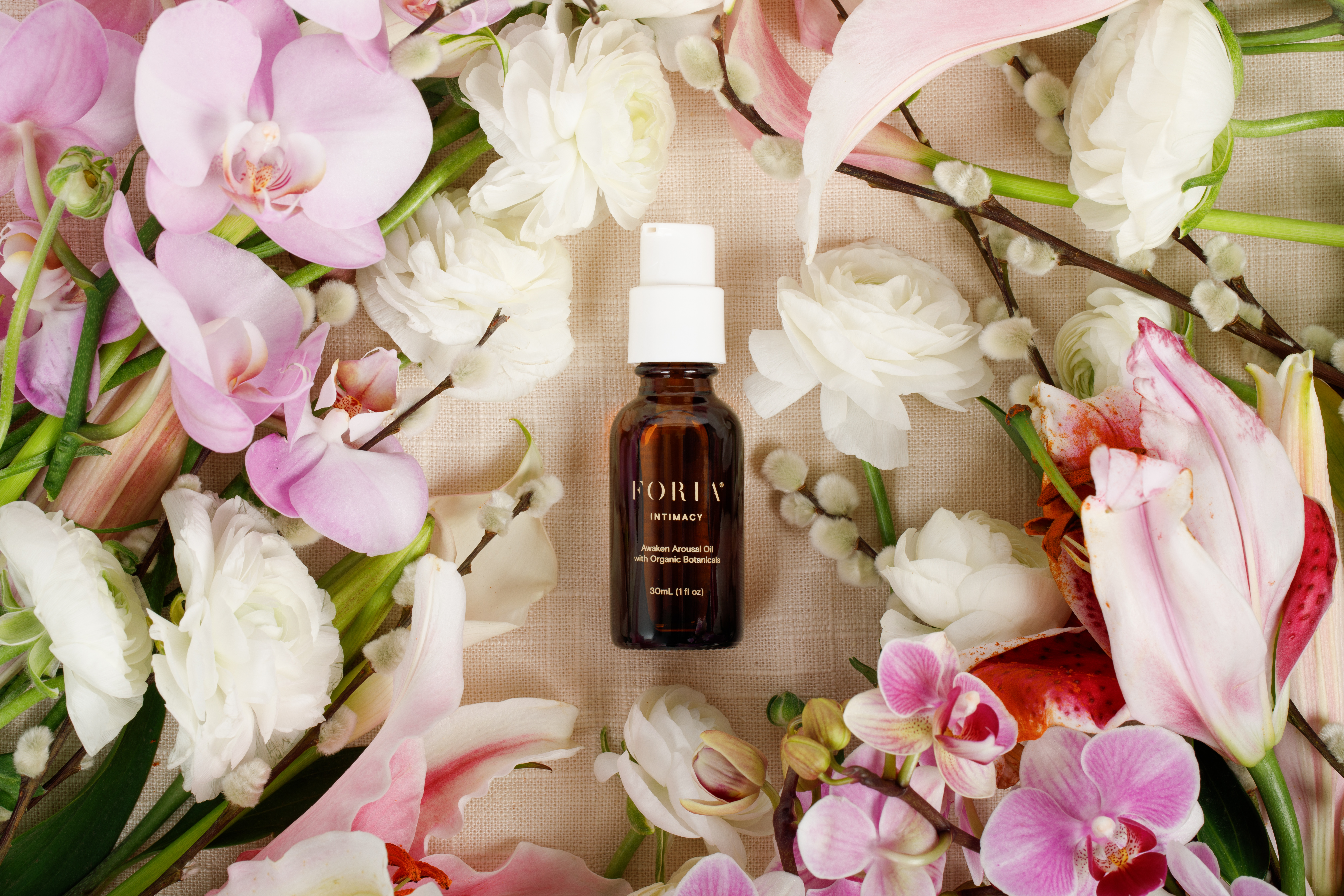 A bottle surrounded by pink and white flowers on a textured surface.