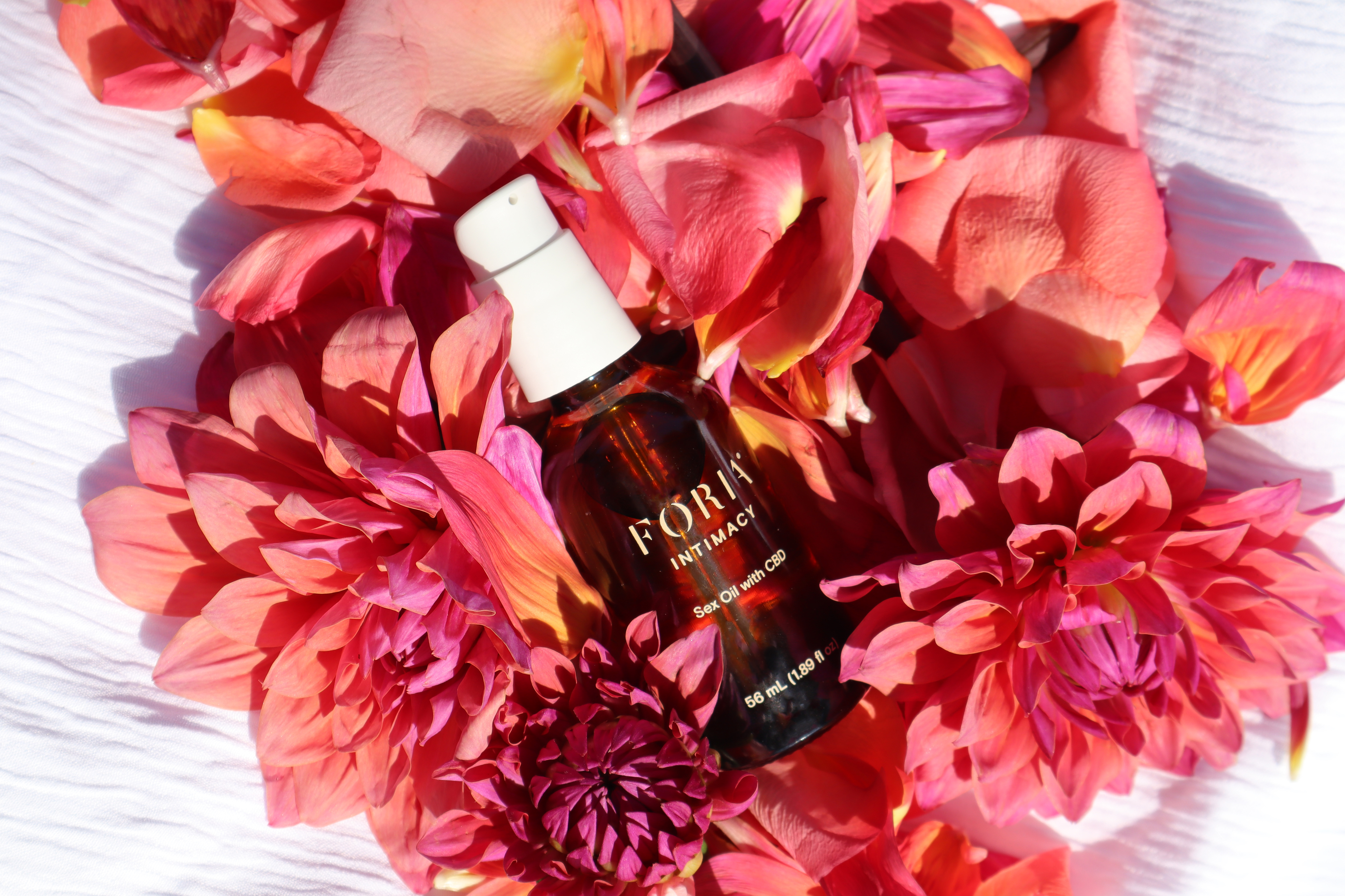 Bottle of oil surrounded by vibrant pink and red flowers.