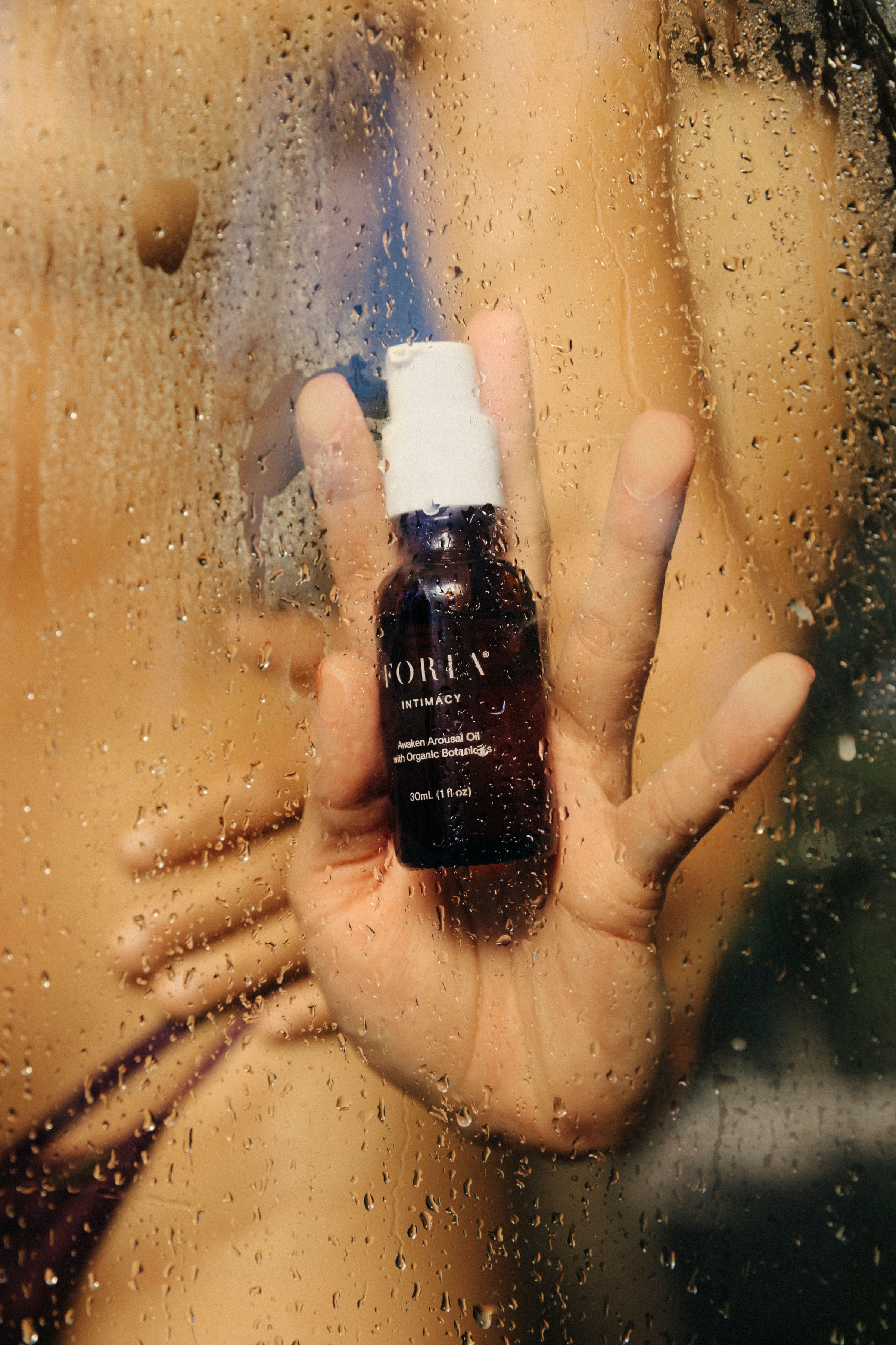 Hand holding a bottle against a steamy, wet glass surface.