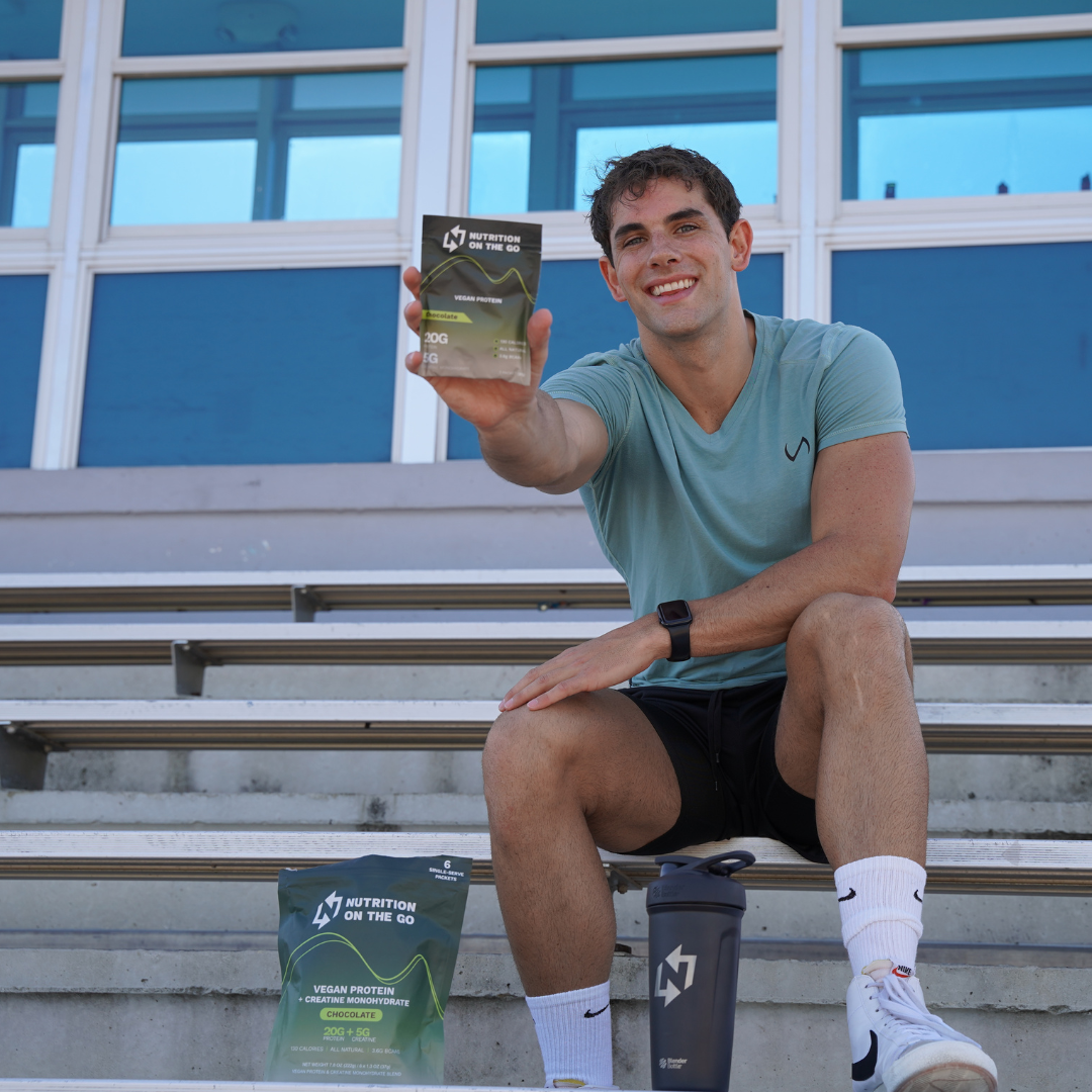 Man sitting on bleachers holding a nutrition packet, with a shaker bottle and bag beside him.