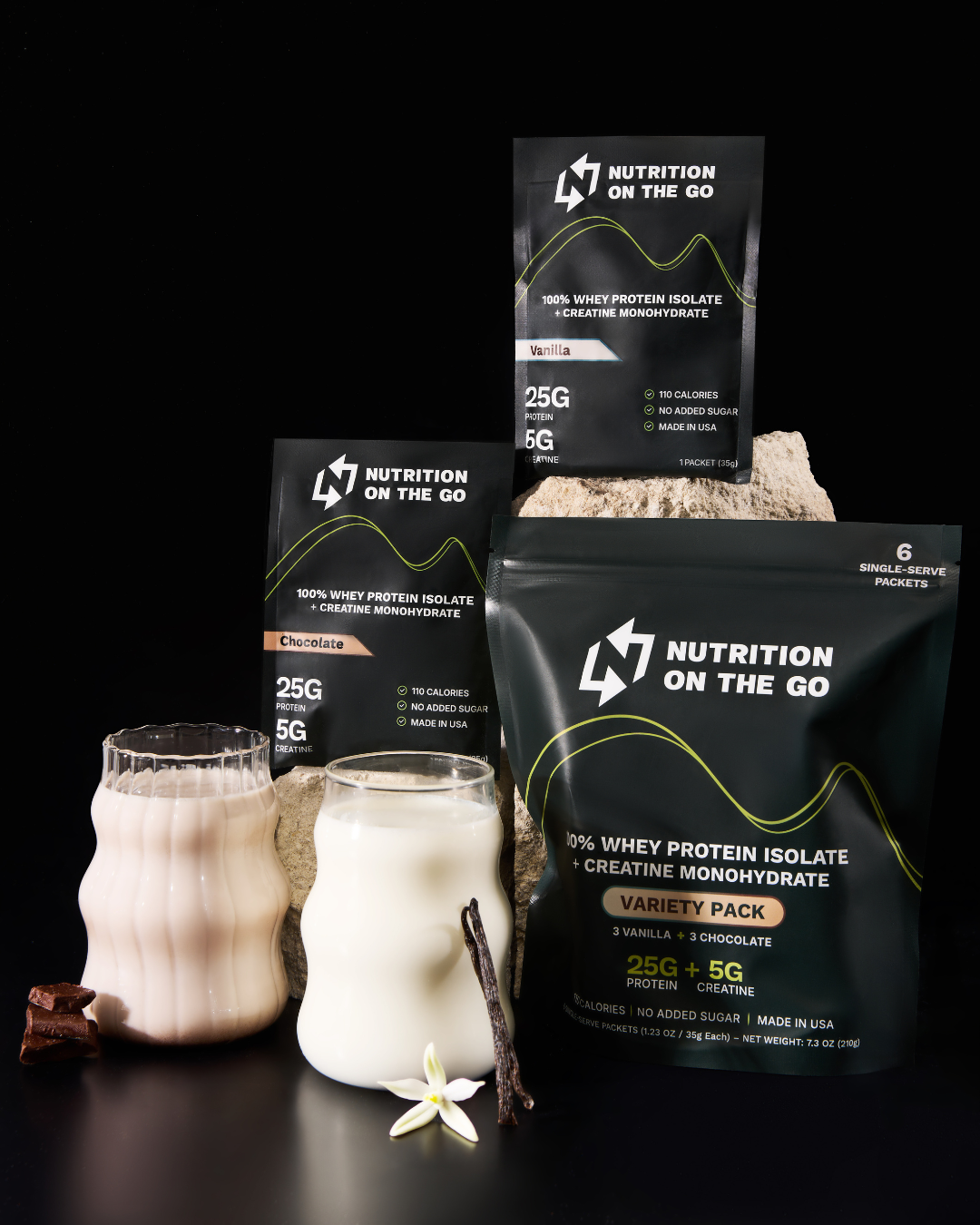 Protein powder packets with glasses of milk, chocolate, and vanilla on a black background.