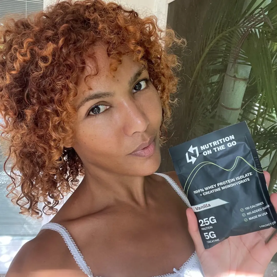 A female smiling and holding a single packet of nutrition on the go protein powder with creatine monohydrate