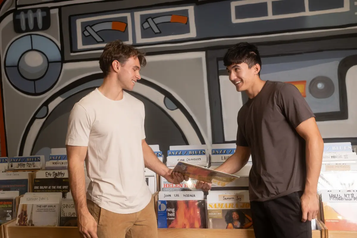 Two men in record shop Man on left wearing Supima Tee in Bone and Man on right wearing Supima Tee in Dark Grey. Shop the full Supima Tee Collectin made from the softest fabric ever: Supima cotton.