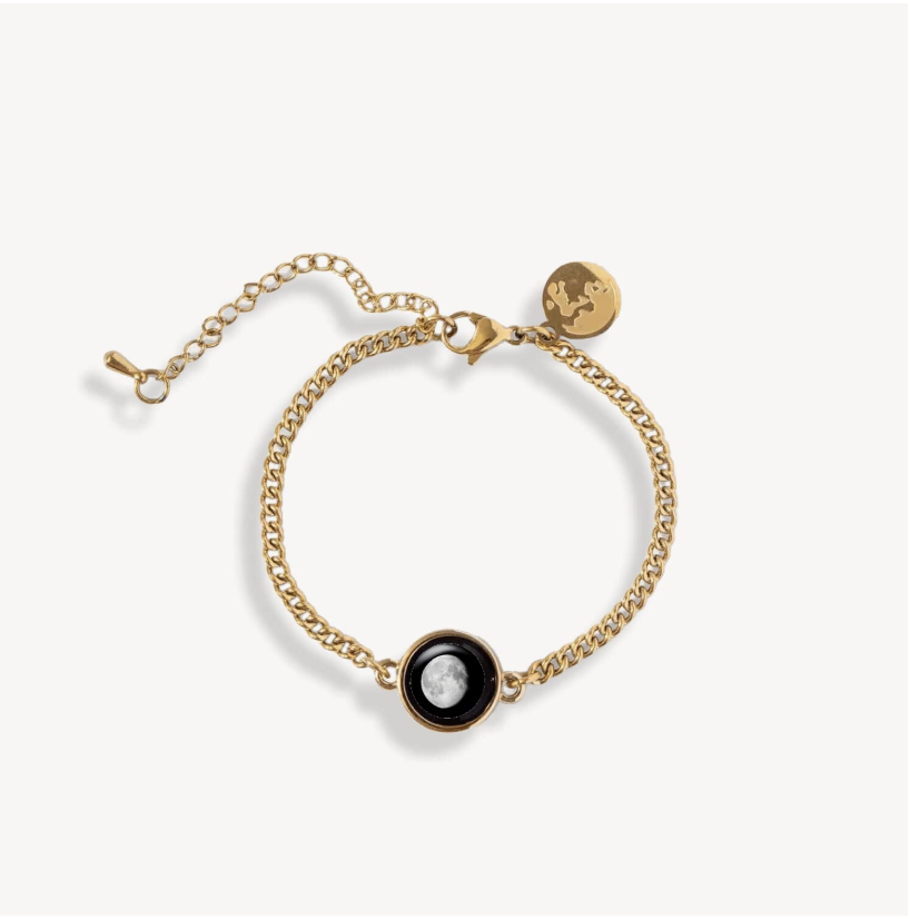 Gold bracelet with a moon phase charm and a small round tag.