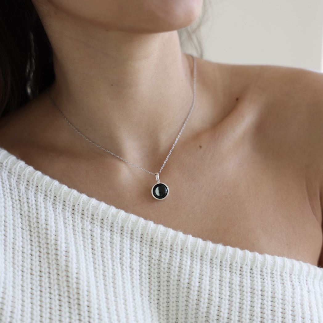 Silver necklace with a blue pendant next to a white flower and a plate.