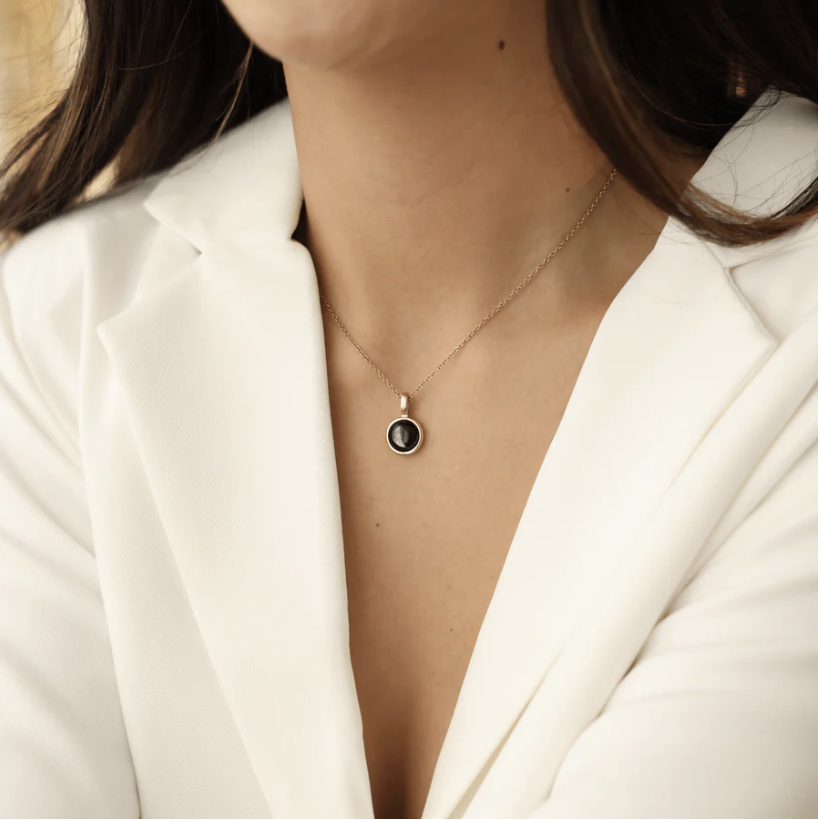 Person wearing a white blazer and a round pendant necklace.