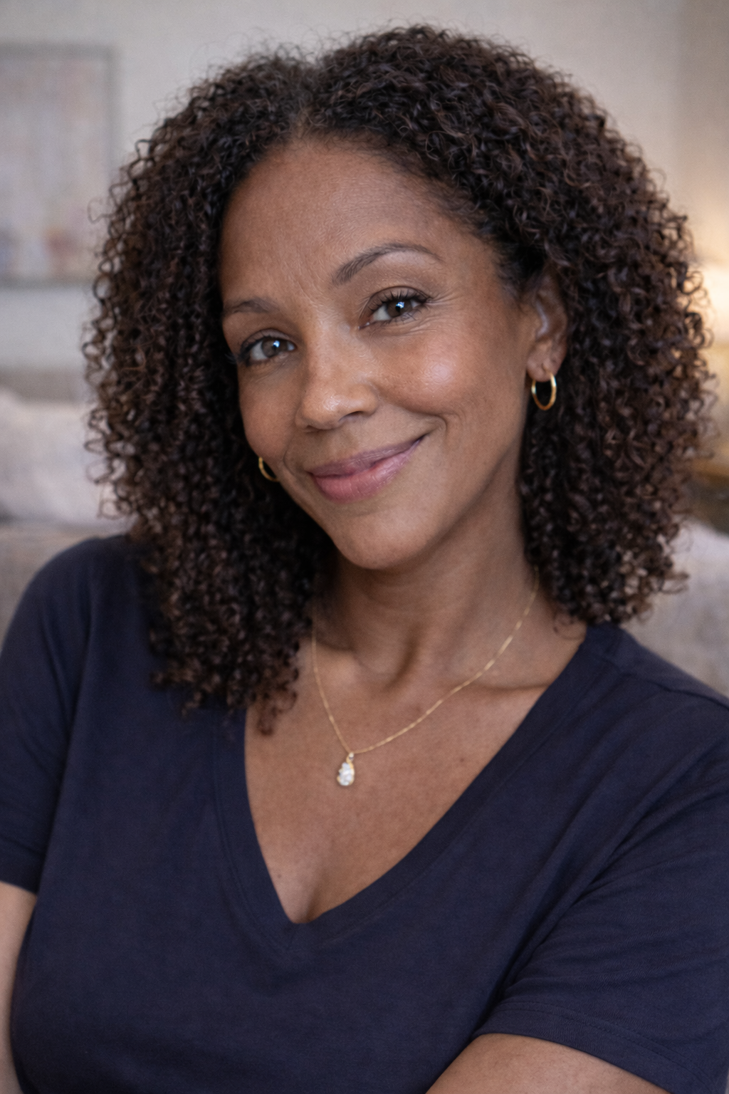 A smiling woman with curly brown hair, wearing a dark blue v-neck shirt, looks toward the camera.