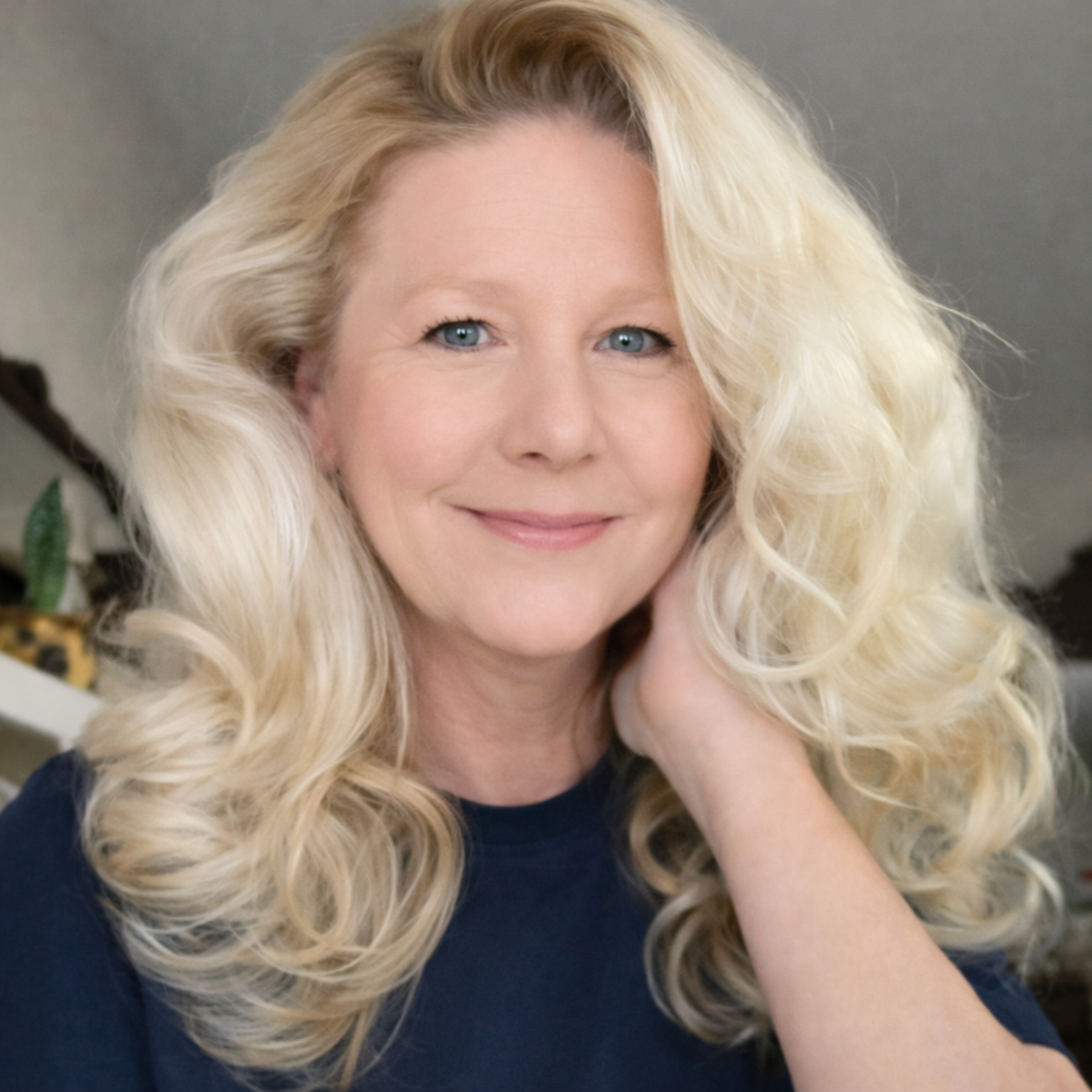 A smiling woman with long, wavy blonde hair and blue eyes, wearing a dark blue shirt.
