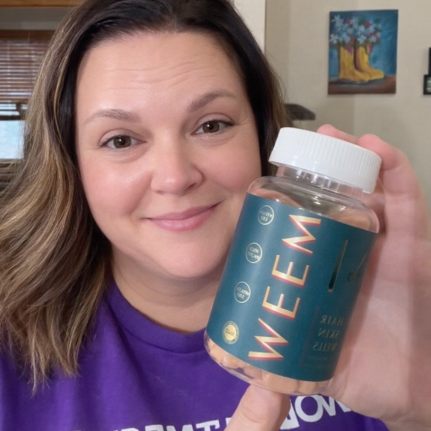 A woman in a purple shirt smiles while holding up a bottle of WEEM supplements.