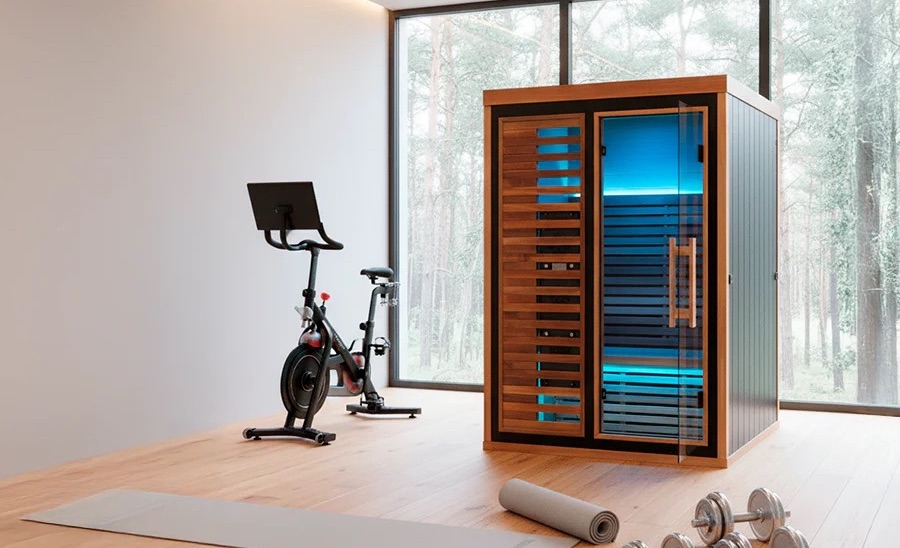 A home gym with an exercise bike, a personal sauna, and weights overlooking a forest.