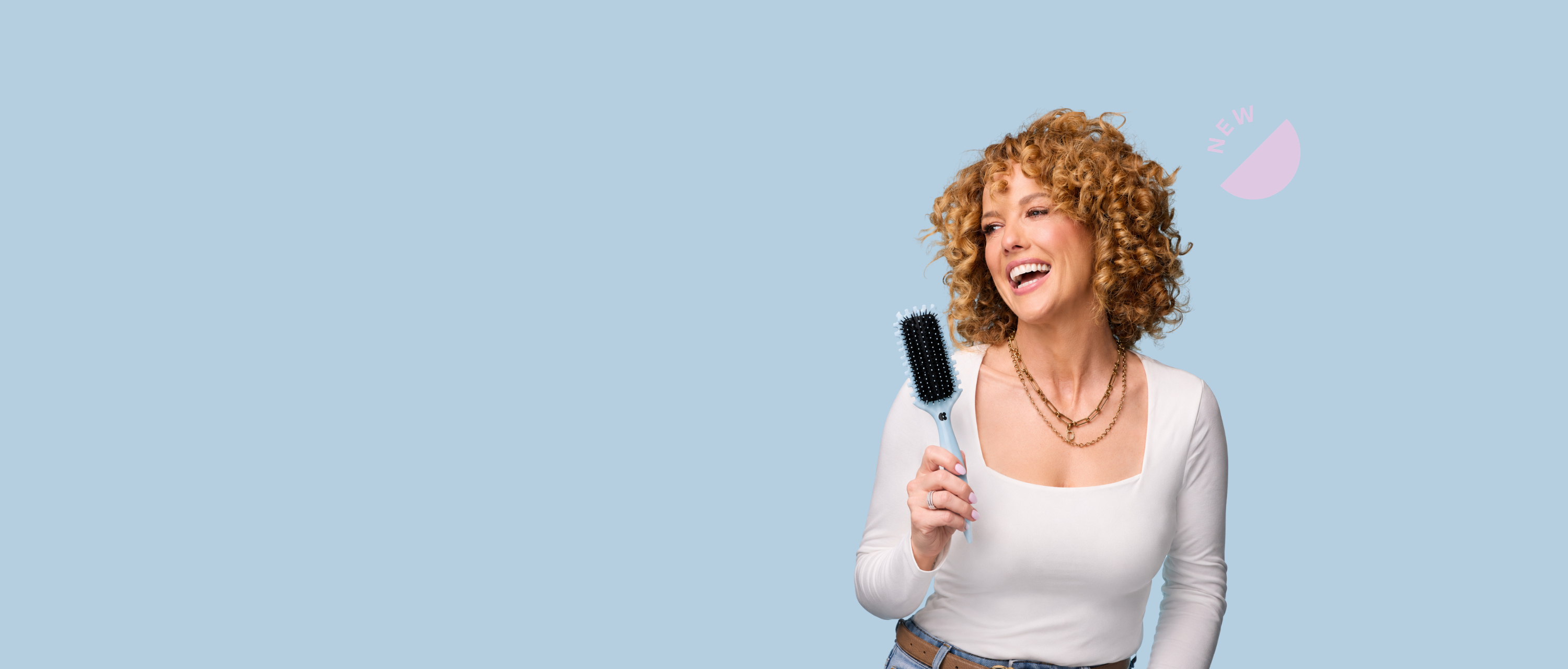 A smiling woman with curly hair holds a light blue hairbrush against a solid light blue background.