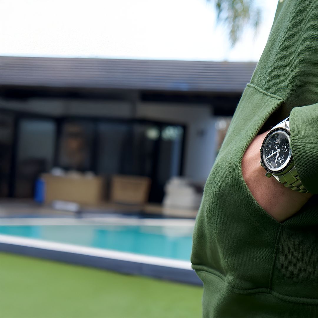 Person in green hoodie with watch, standing by a pool.