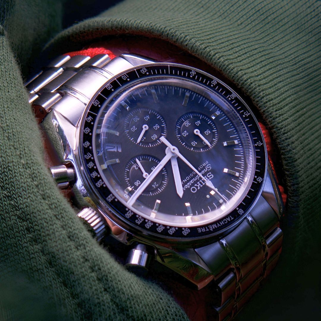 Silver wristwatch with a black dial and multiple subdials, partially covered by green fabric.