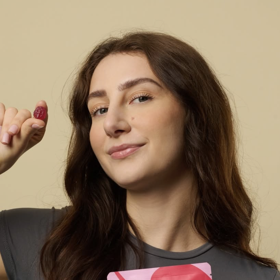Person holding a small red object between fingers, smiling.