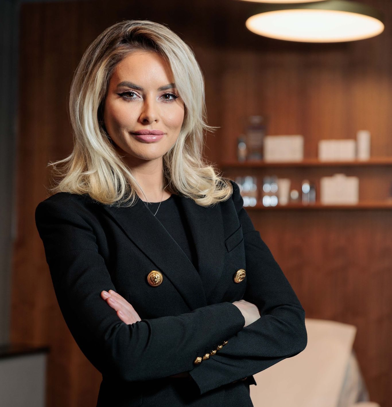 Person with blonde hair in a black blazer standing in an office.
