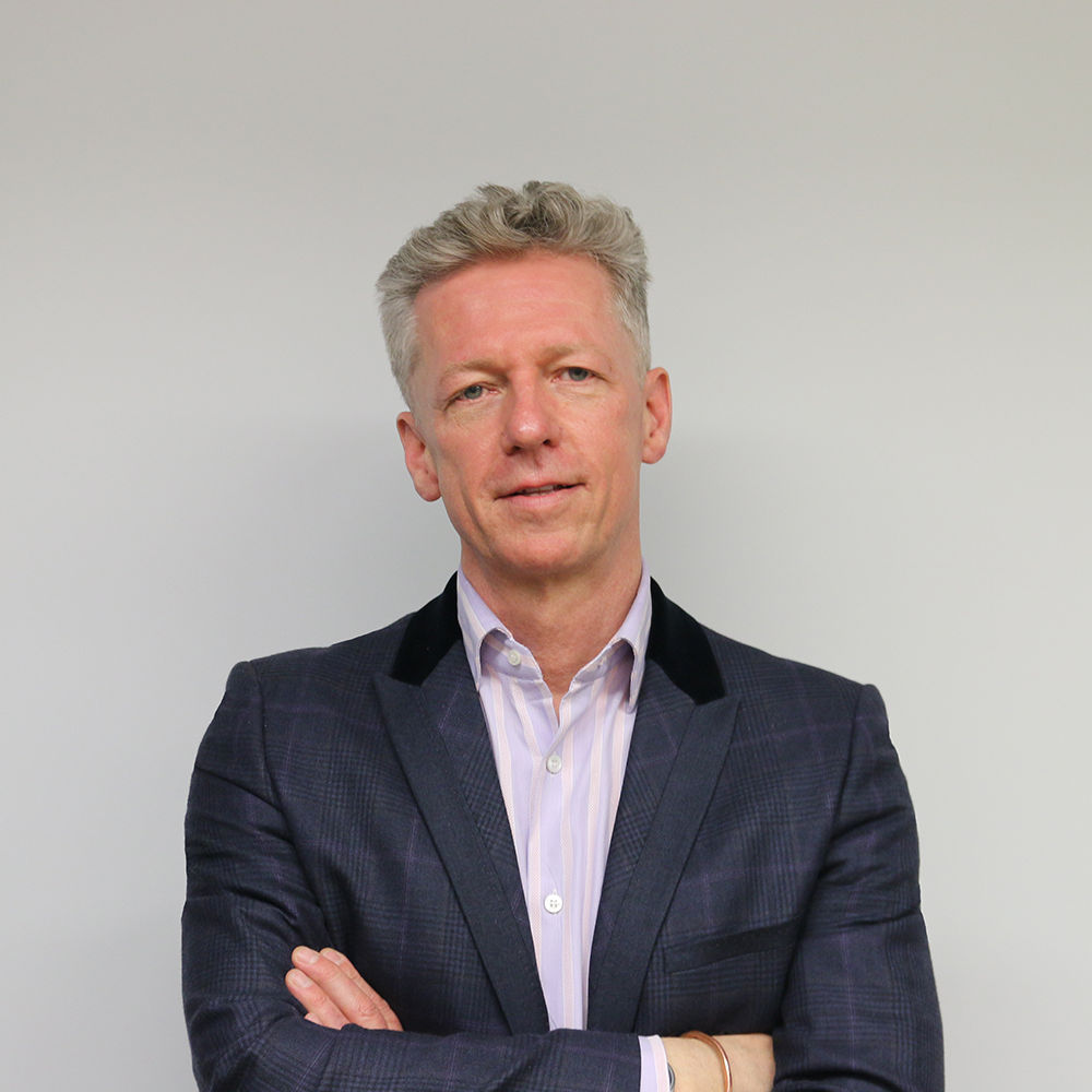 Man in a suit with crossed arms against a plain background.