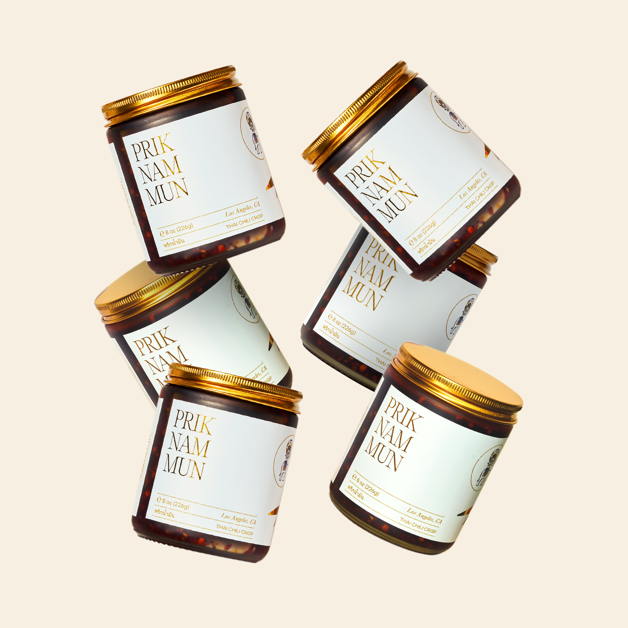 Multiple jars of Prik Nam Mun Thai Chili Crisp scattered against a cream-colored background.