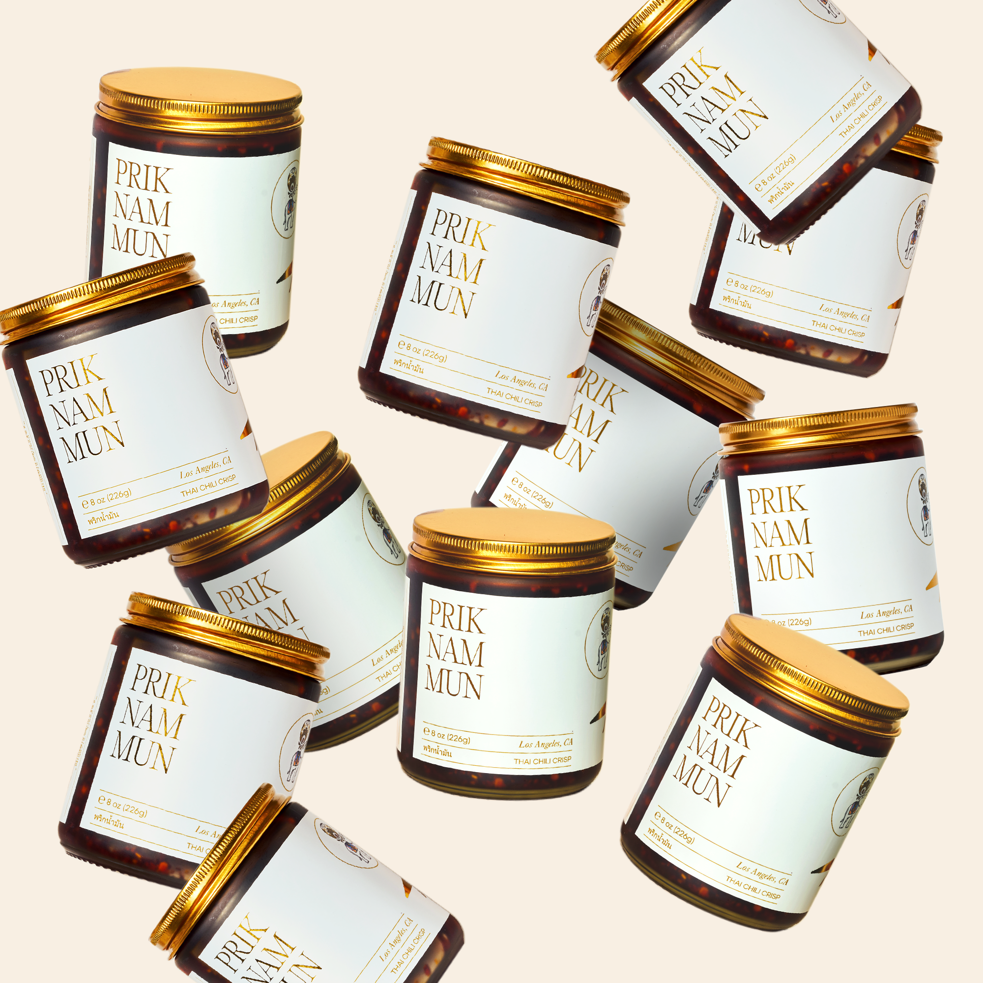 Multiple jars of Prik Nam Mun Thai Chili Crisp with gold lids scattered against a light background.