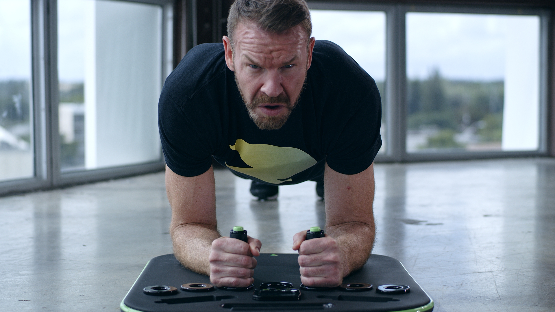 A man with an intense expression holds a plank on a piece of exercise equipment indoors.