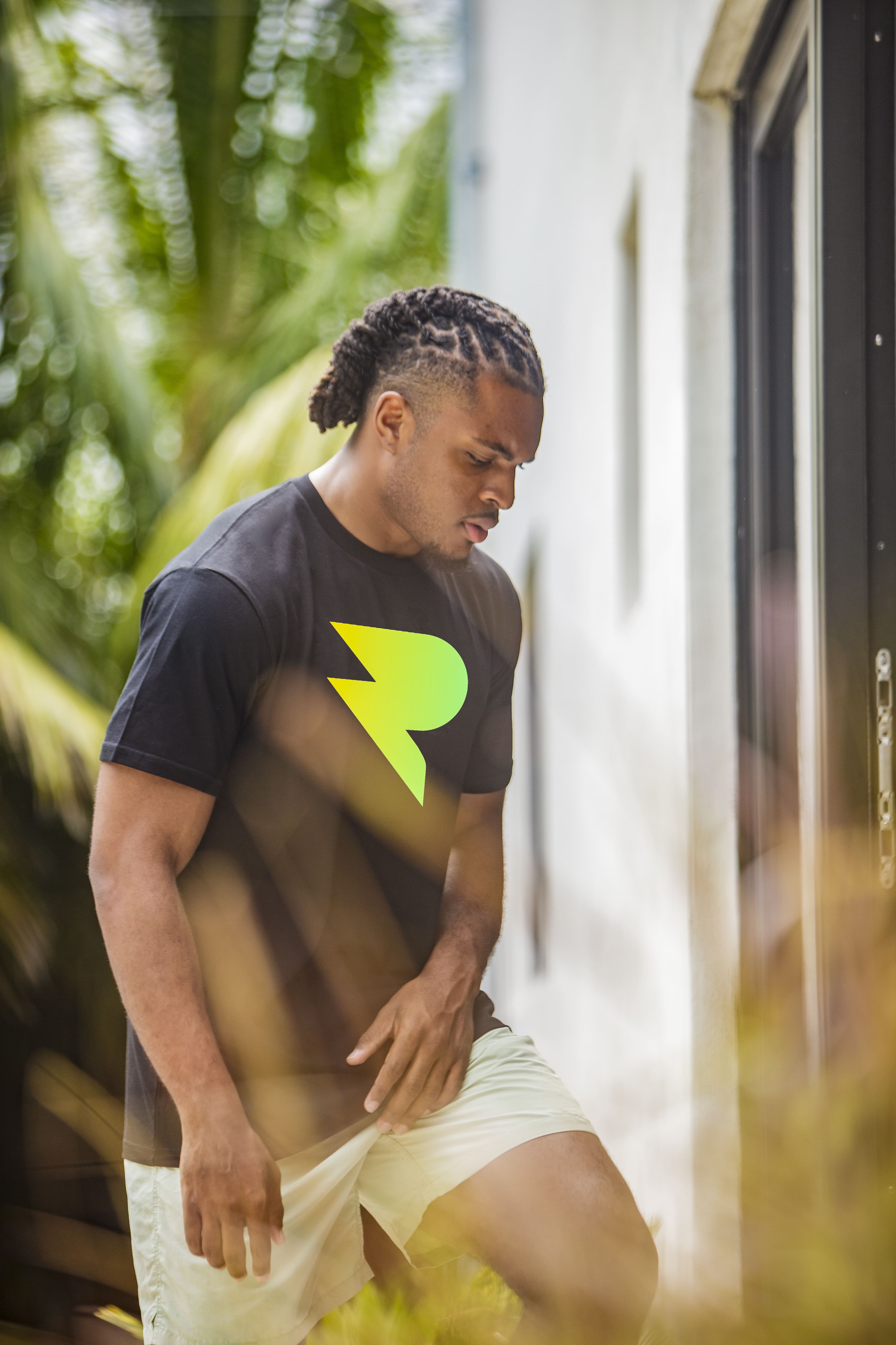 Person in black shirt with yellow logo, standing outdoors near a building.