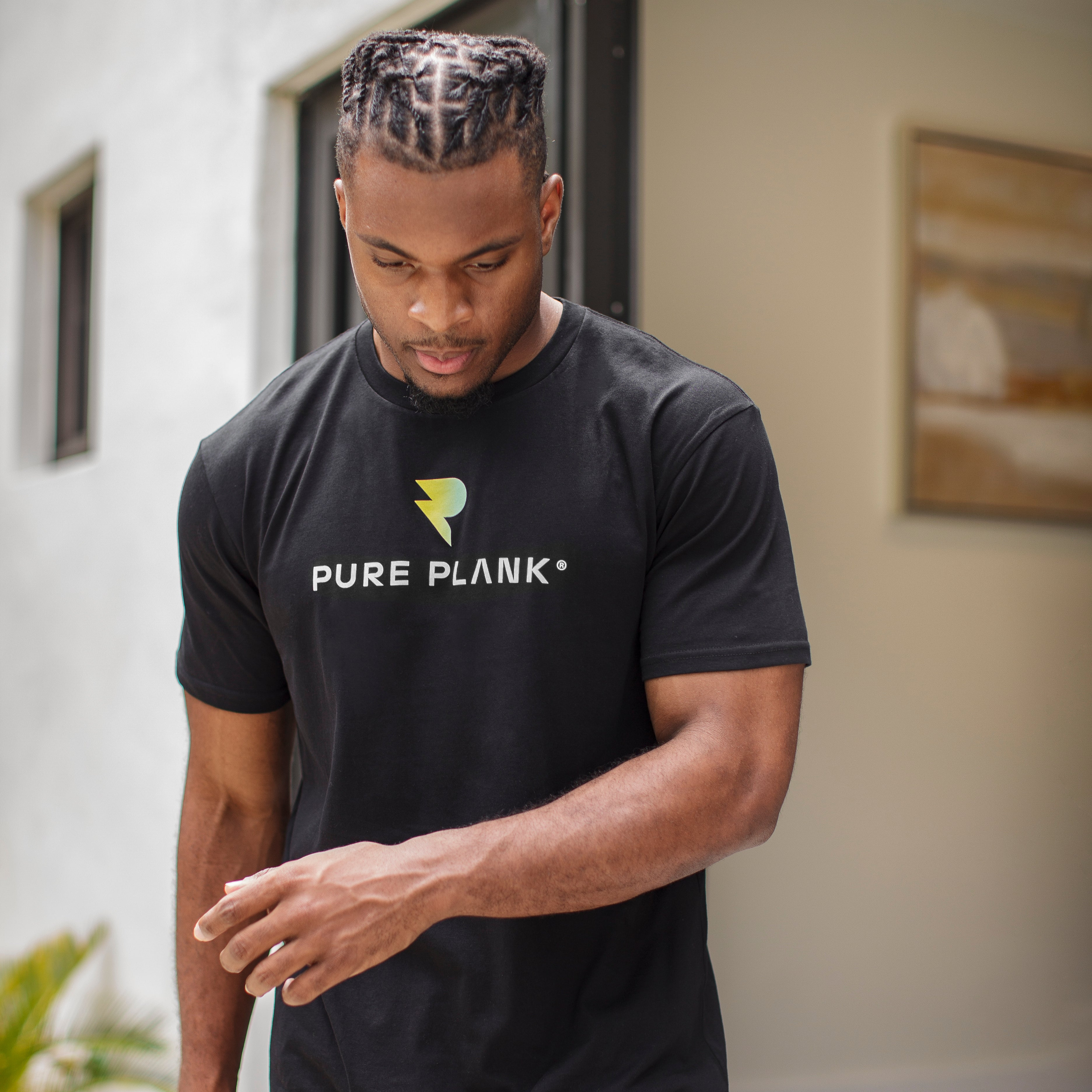 Man in black 'Pure Plank' t-shirt looking down, standing indoors.