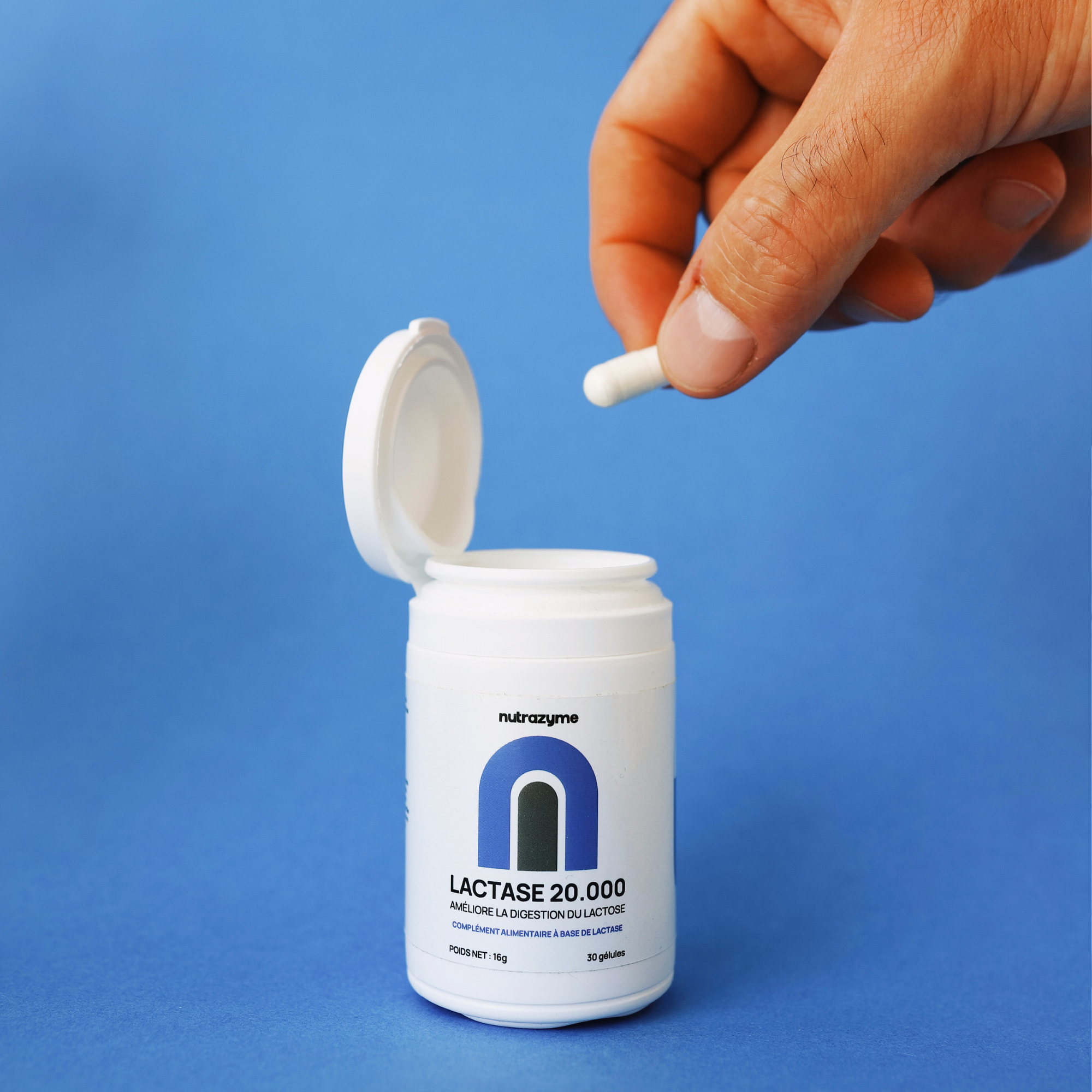 Hand holding a capsule above an open lactase supplement bottle.