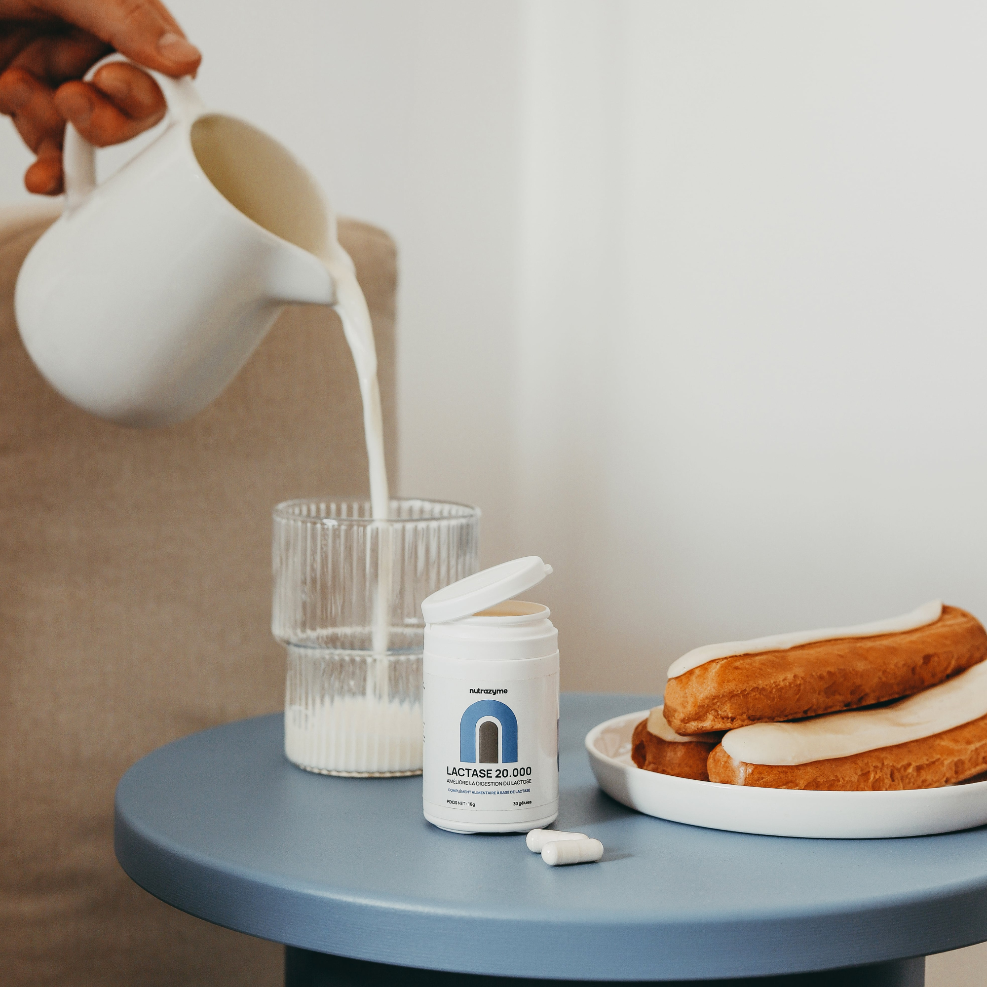 Milk being poured into a glass beside lactase pills and pastries.