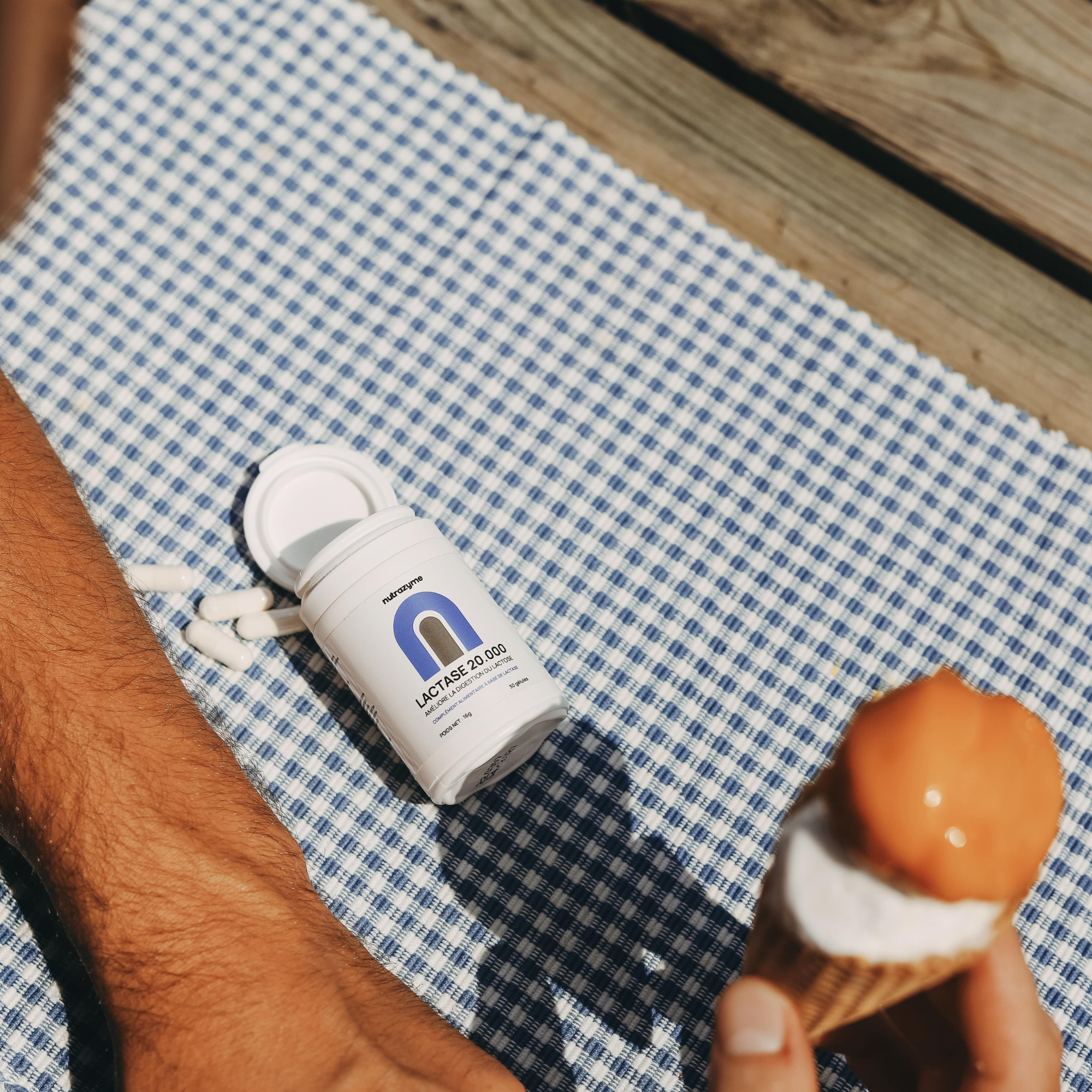 Lactase supplement bottle on checkered cloth with ice cream cone and arm visible.