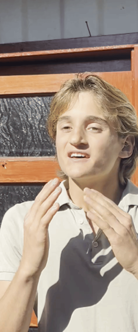Person gesturing with hands in front of a wooden structure.