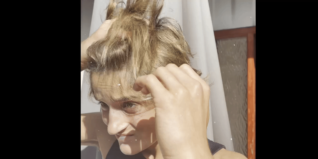 Person adjusting their hair outdoors in sunlight.