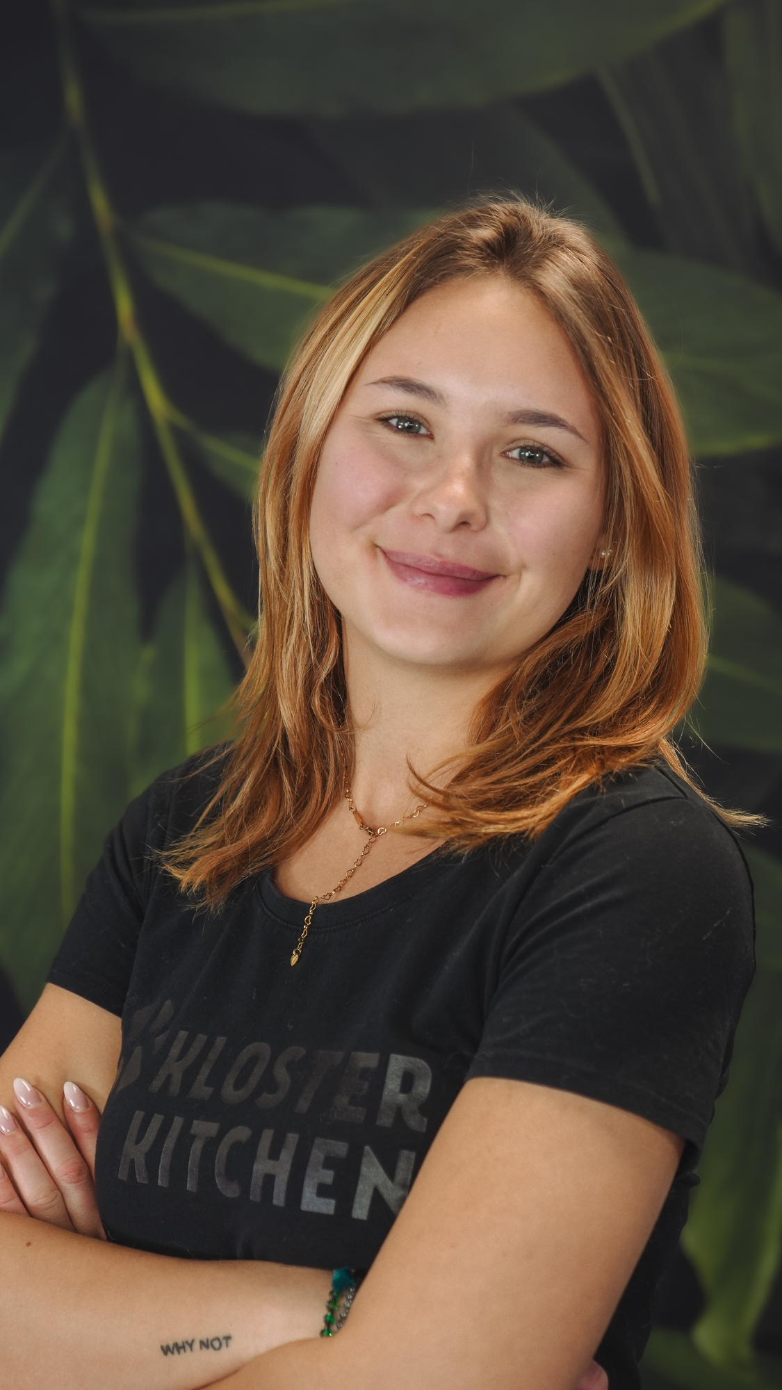 A person smiling in front of a leafy background.