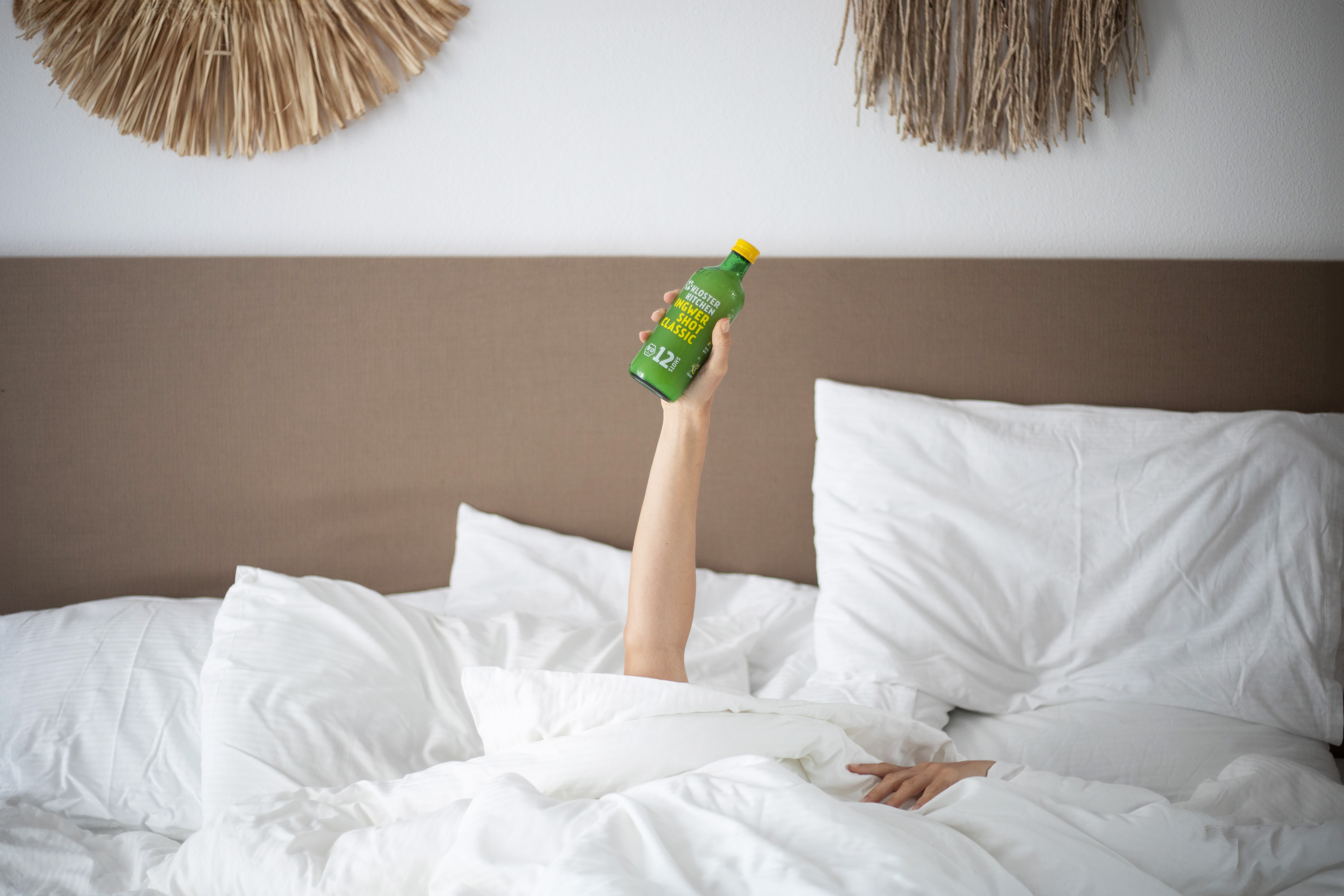 Person in bed holding up a green juice bottle.