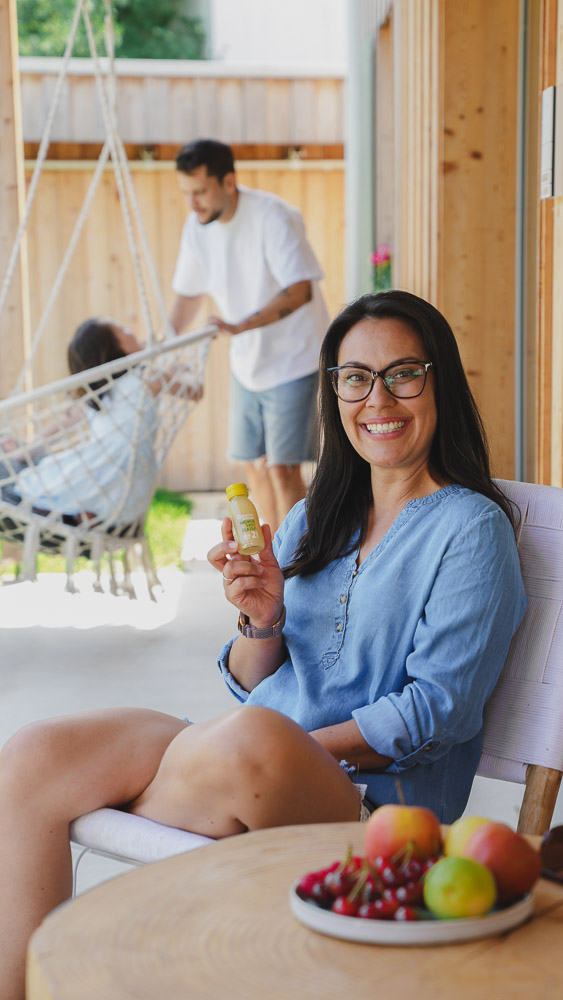 Woman smiling, holding a bottle; background shows a man and woman on a swing.