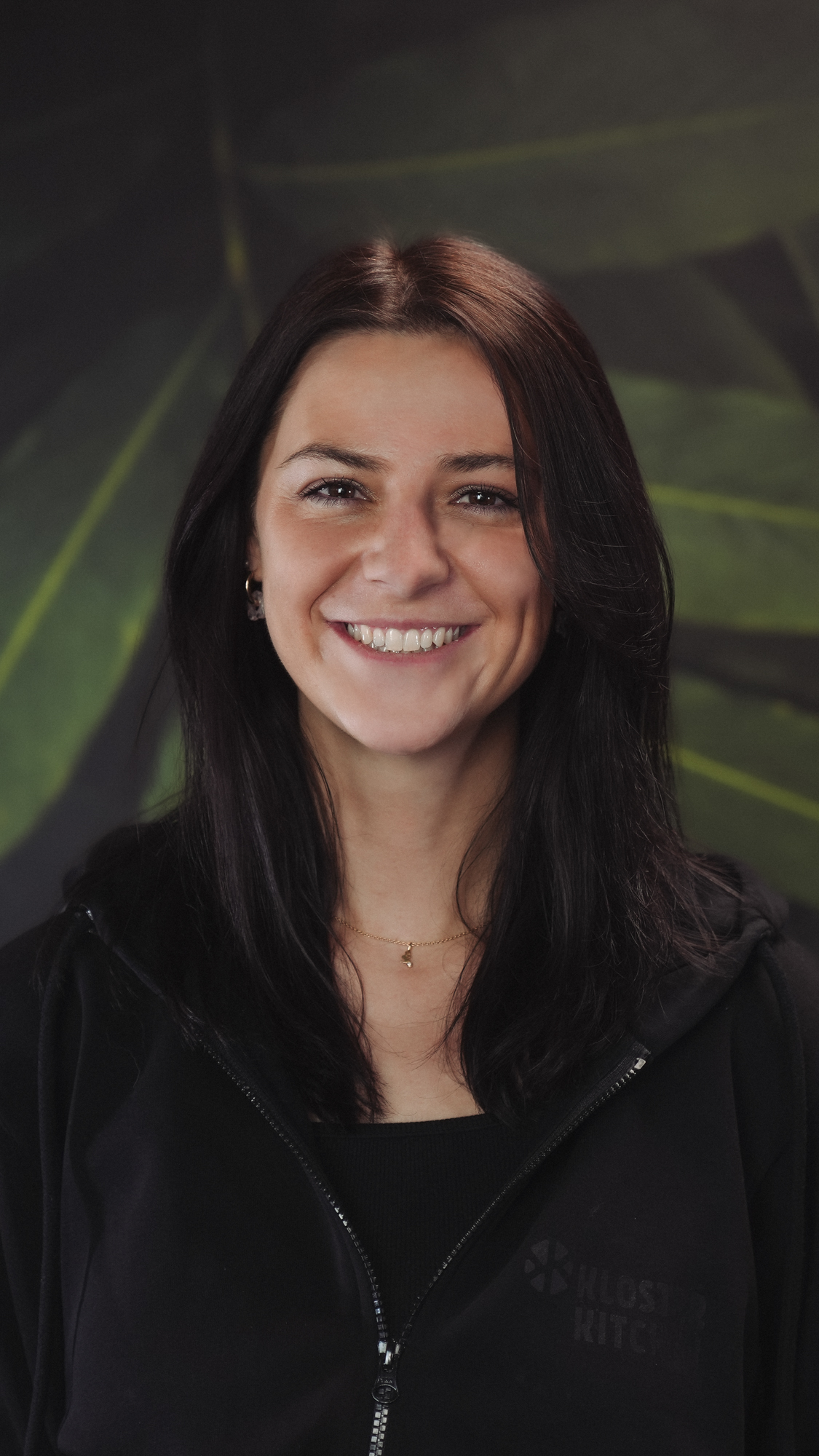 Smiling woman with dark hair against a leafy green background.