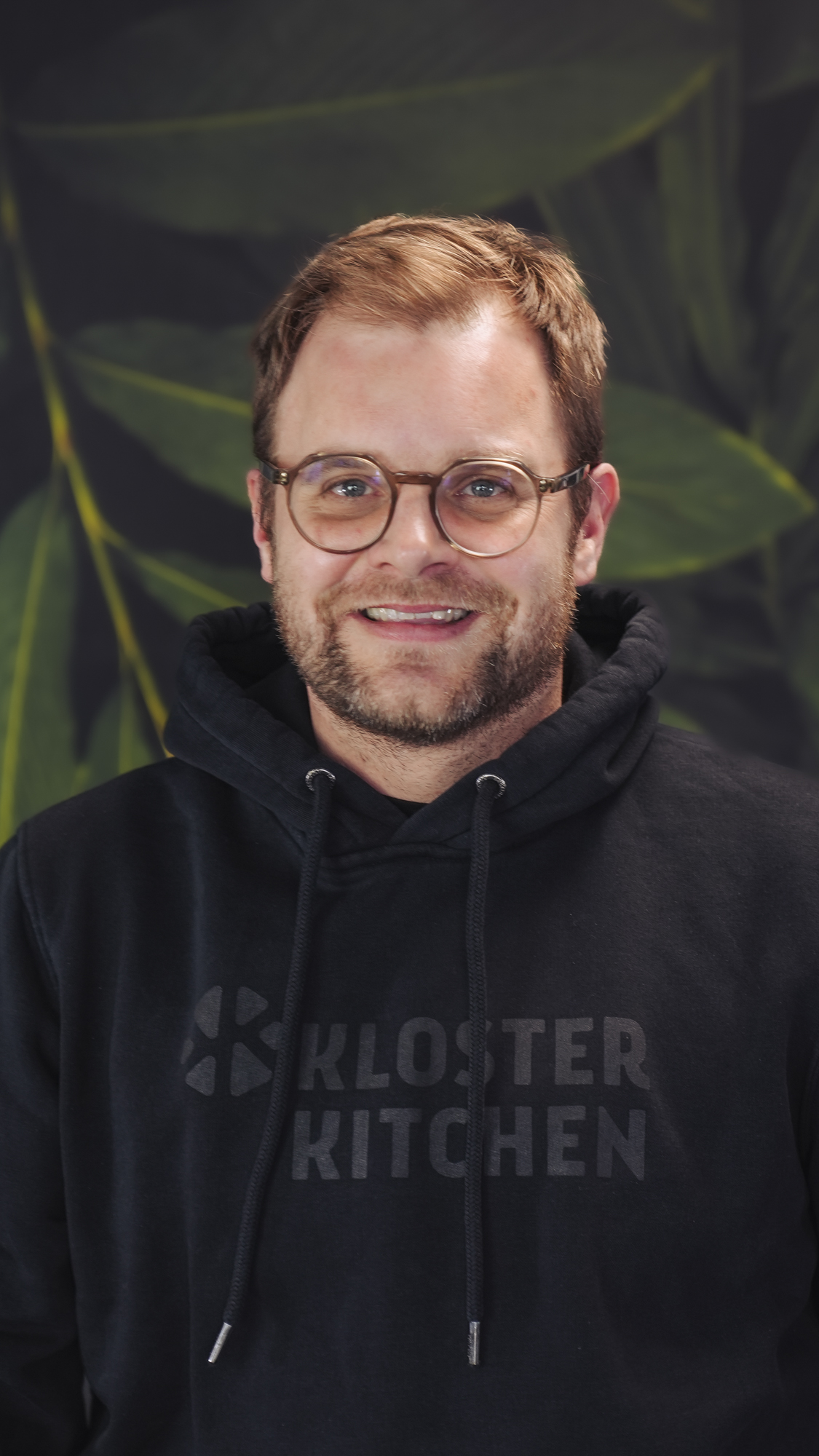 Man in glasses wearing a black hoodie withKloster Kitchen' text.