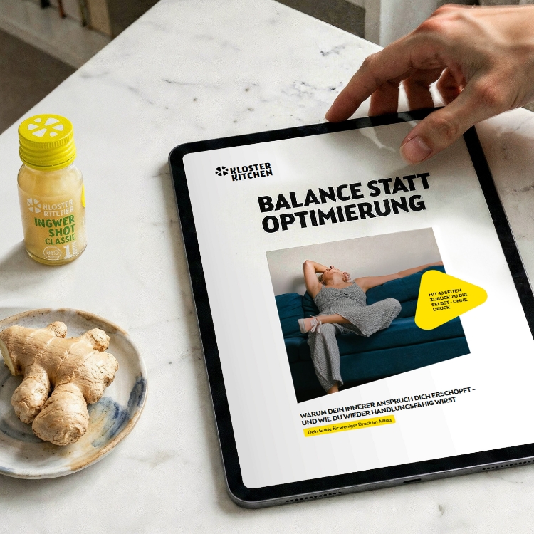 A tablet on a marble table displays a document next to a ginger shot and fresh ginger root.