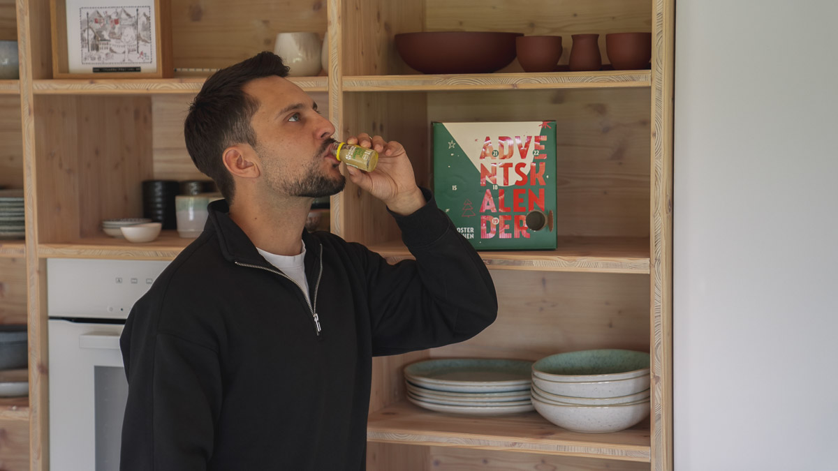 Man drinking from a bottle in front of wooden shelves.