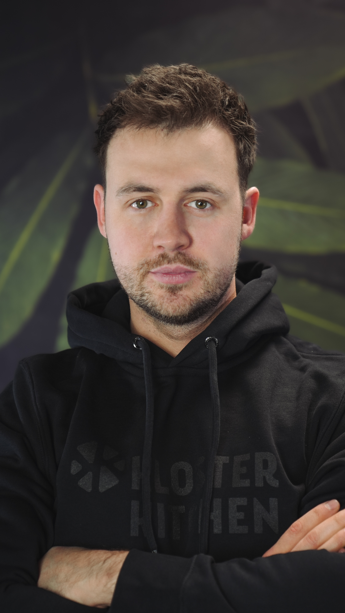 A person in a black hoodie with a nature-themed background.