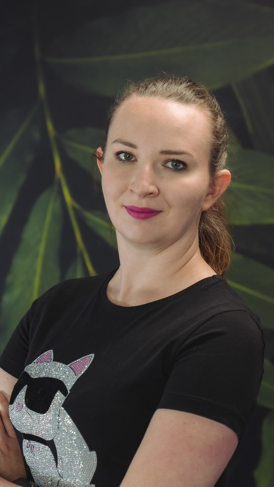 A person with a black shirt standing against a leafy background.