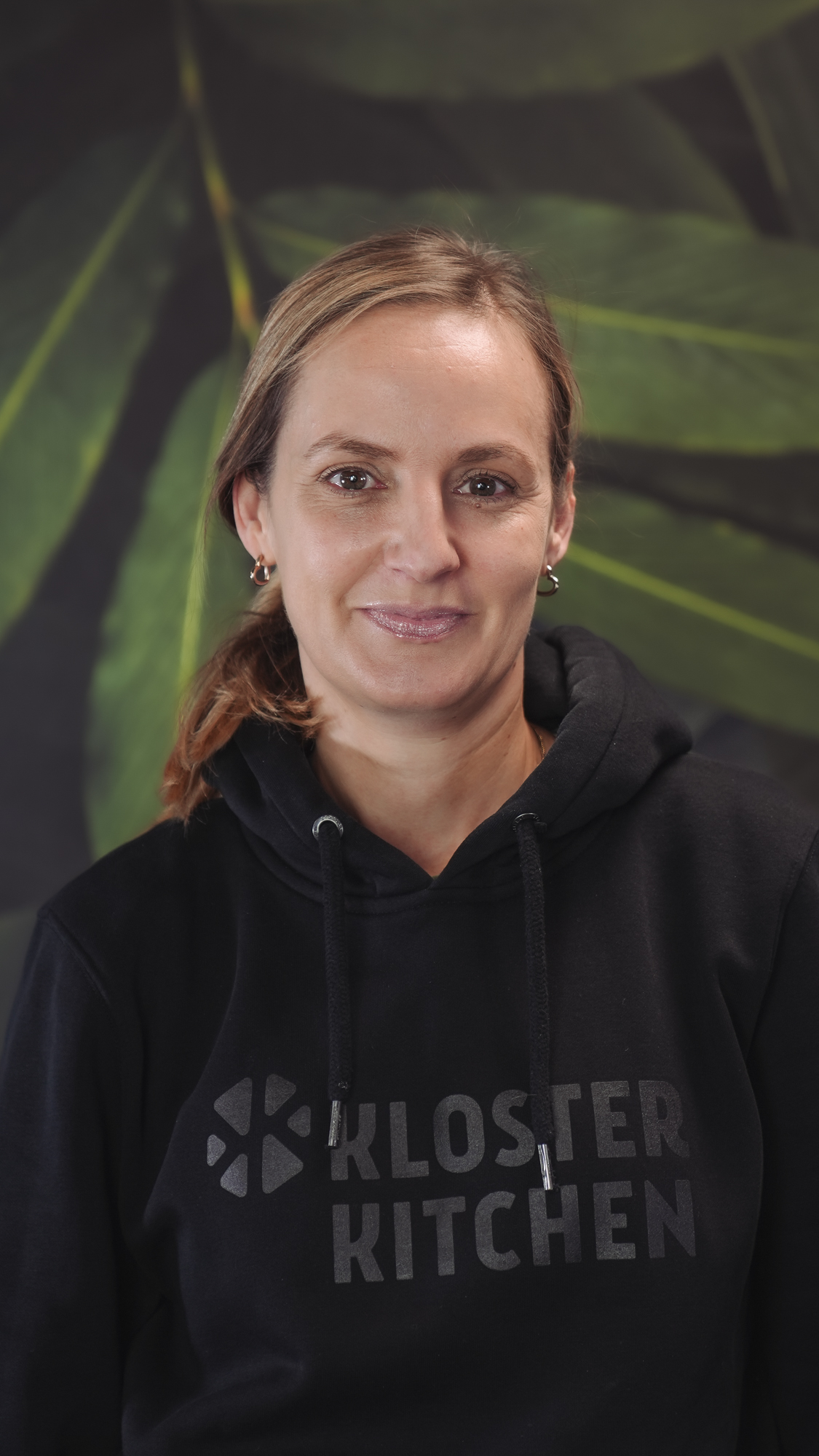 A person in a black hoodie with a green leaf background.