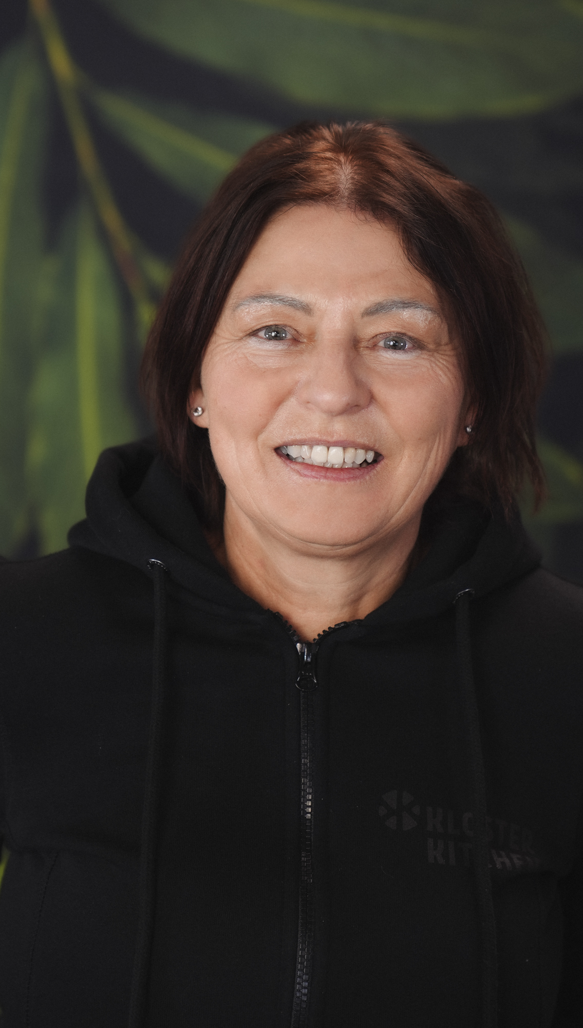 Smiling person in a navy-blue shirt with a leafy background.