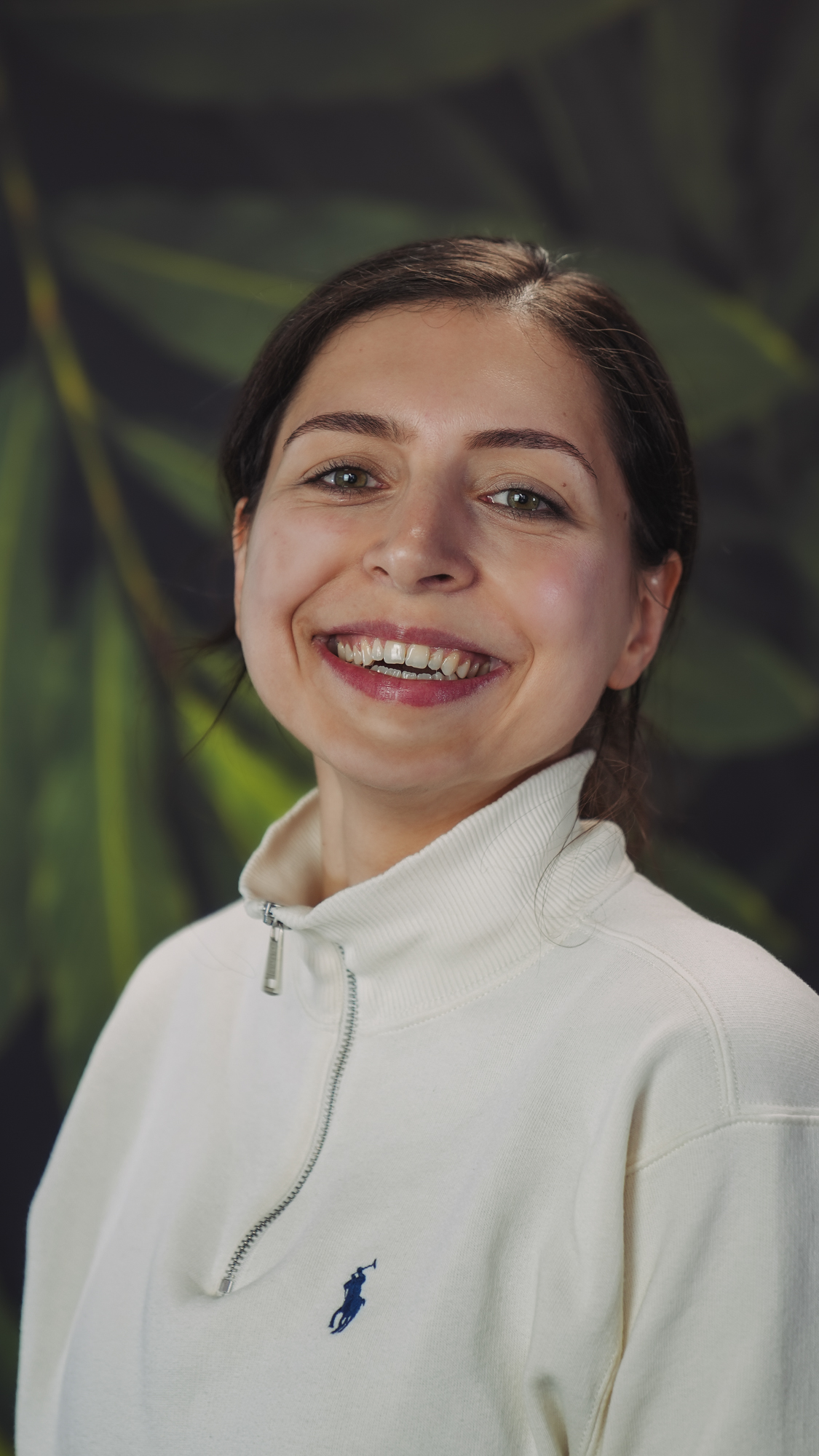 Smiling person with dark hair against a leafy background.