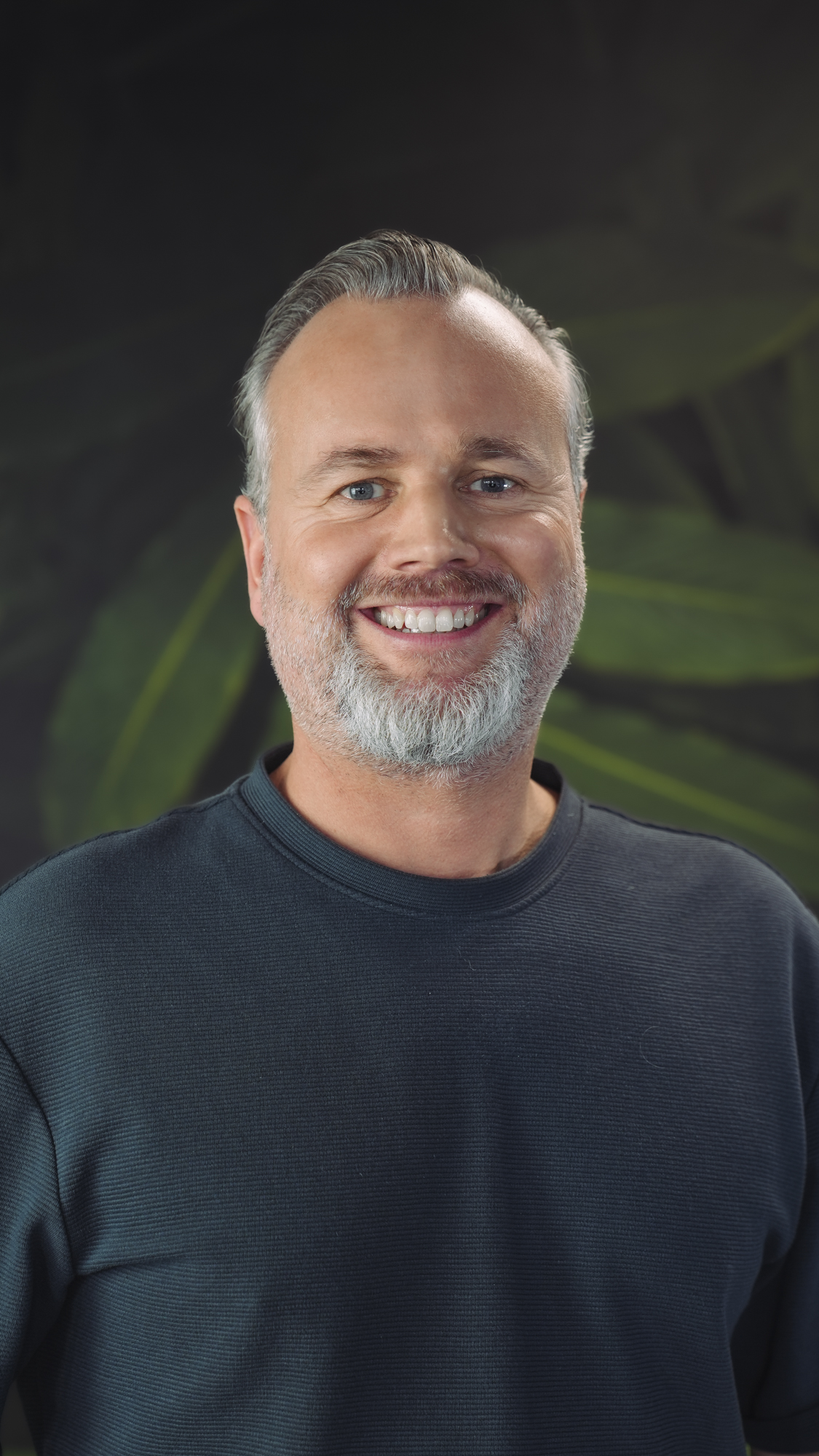 Man in a black hoodie with a nature-themed background.