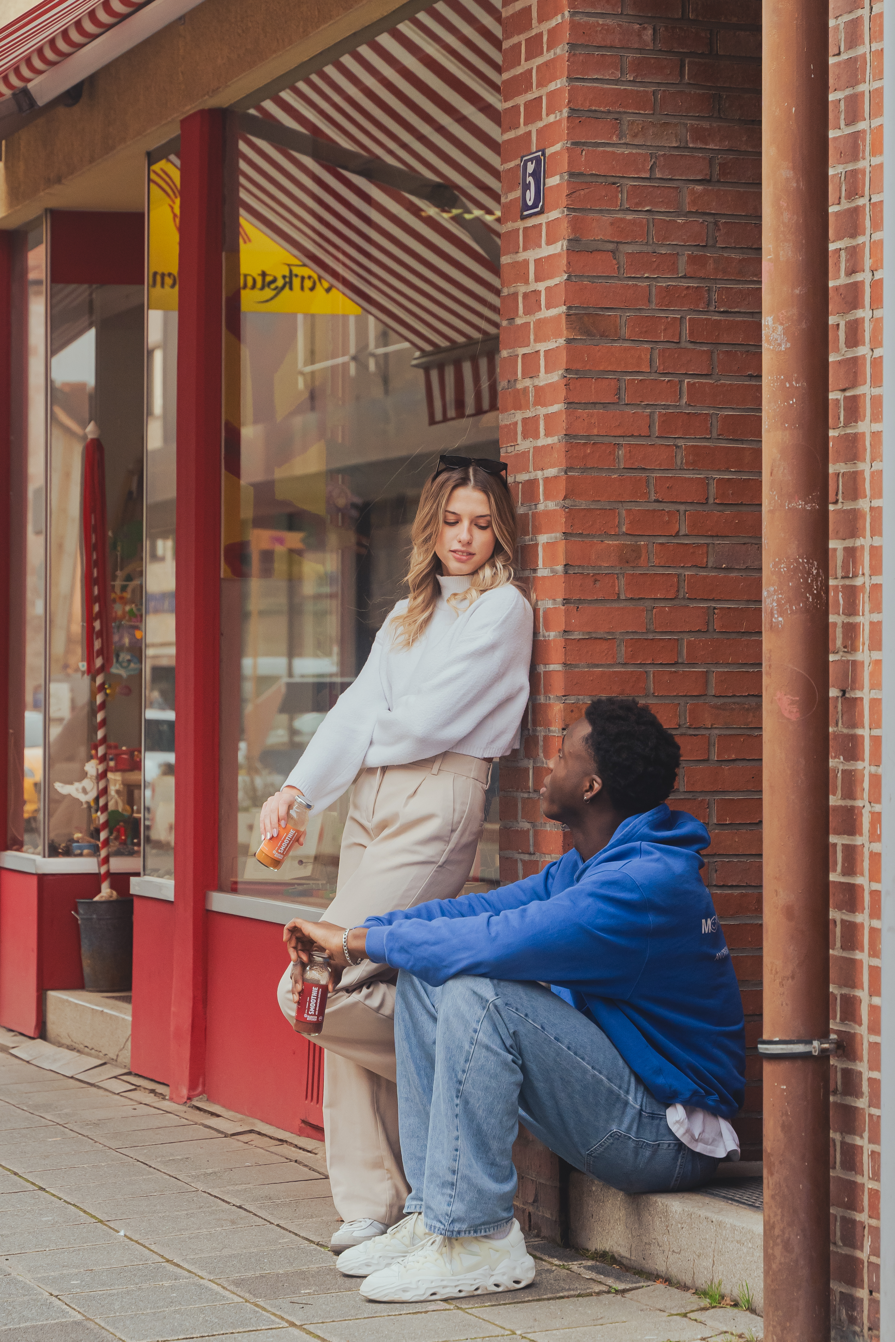 A woman and man talking outside a brick storefront with drinks.