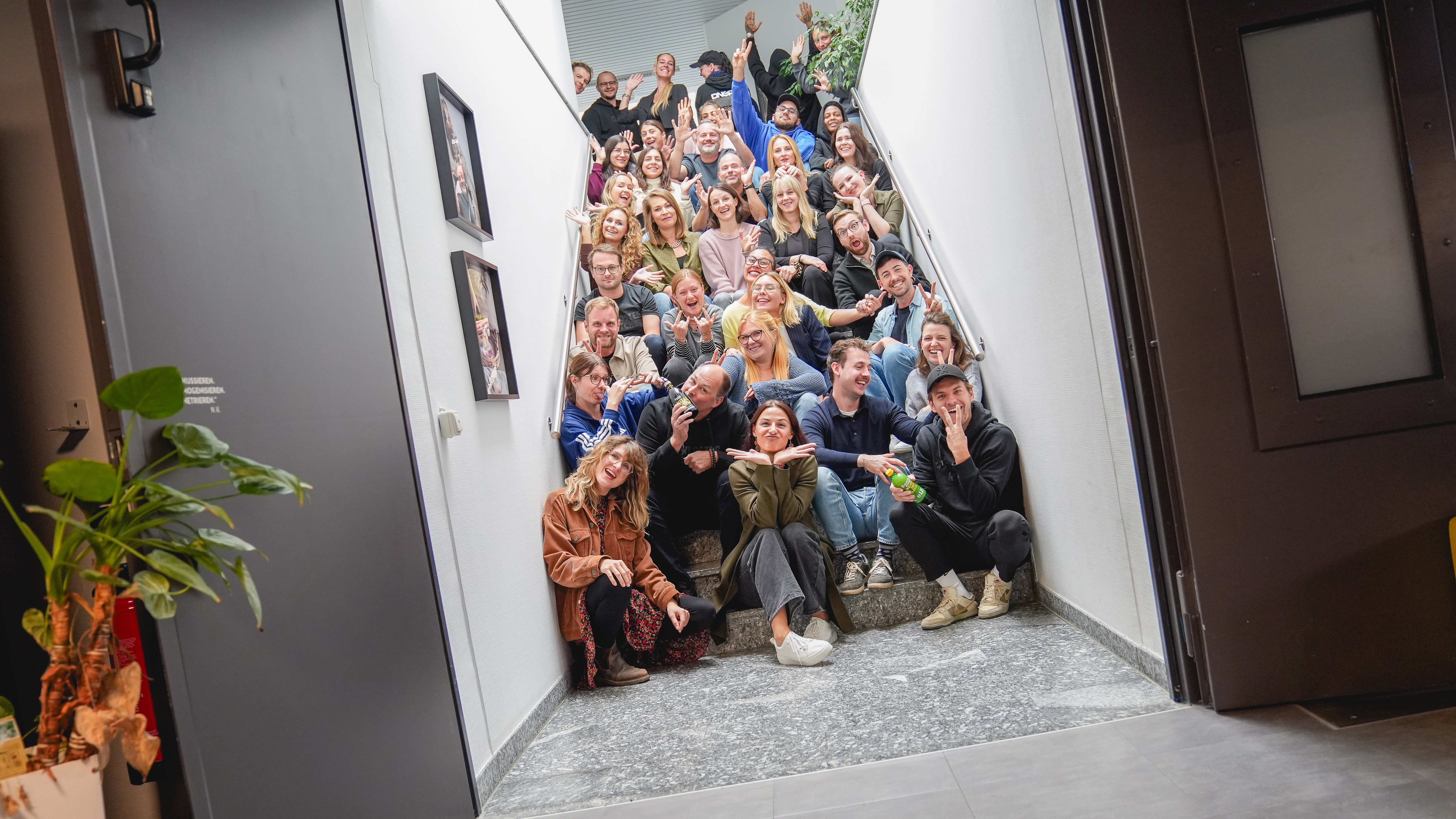 Gruppo di persone in posa sulle scale, sorridenti e che fanno gesti.