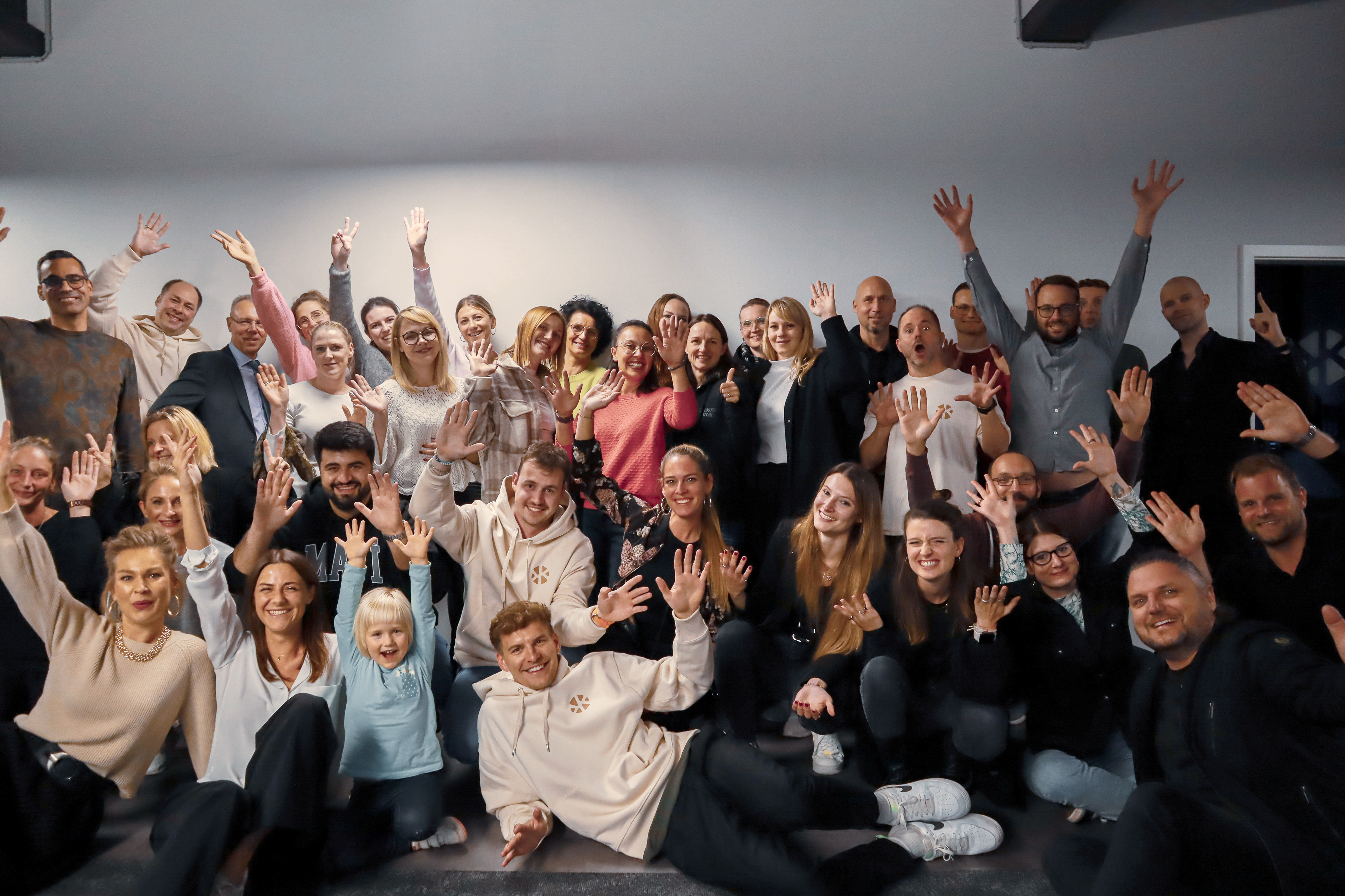 Group of people raising hands and smiling in a cheerful pose.