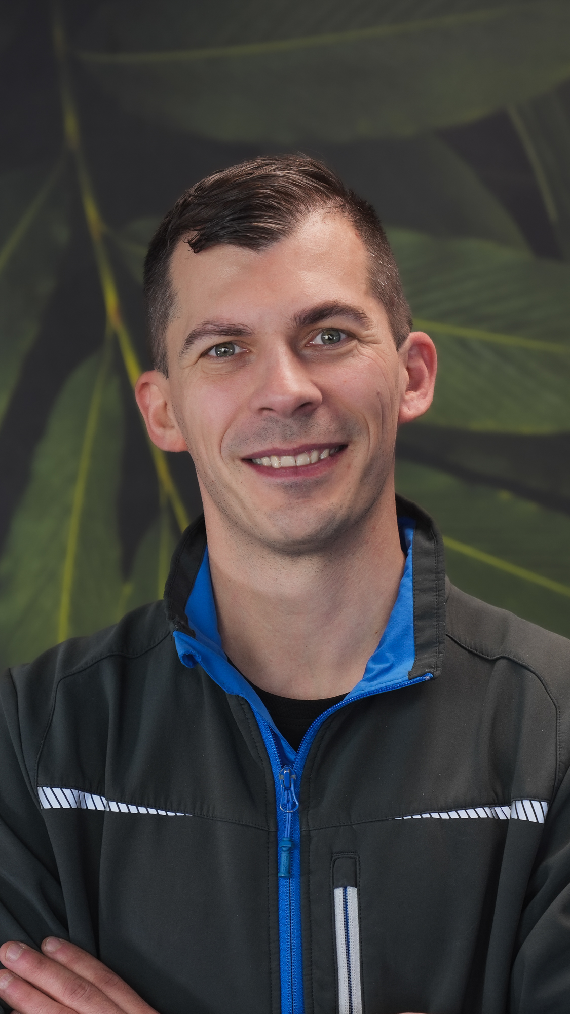 Man smiling in front of a leafy background.