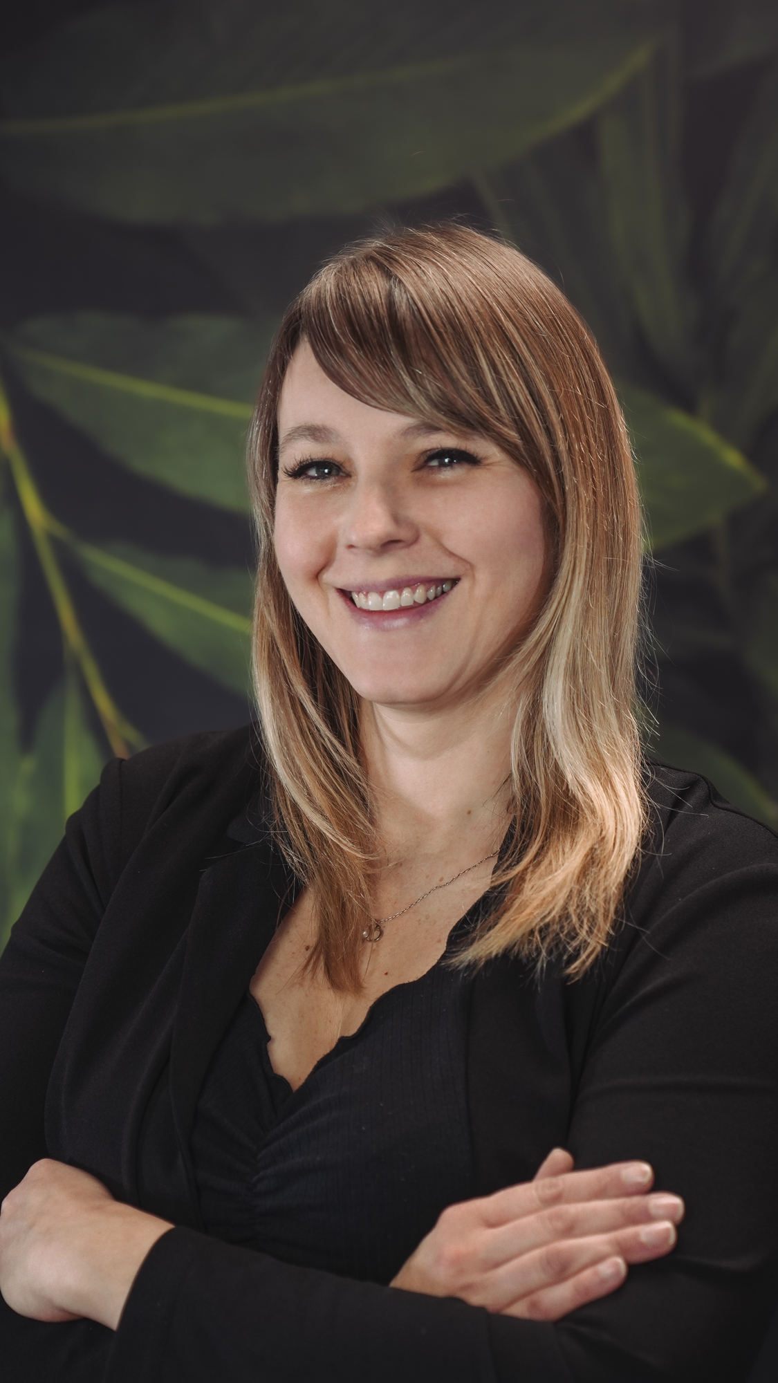 Smiling person with blonde hair against a leafy background.